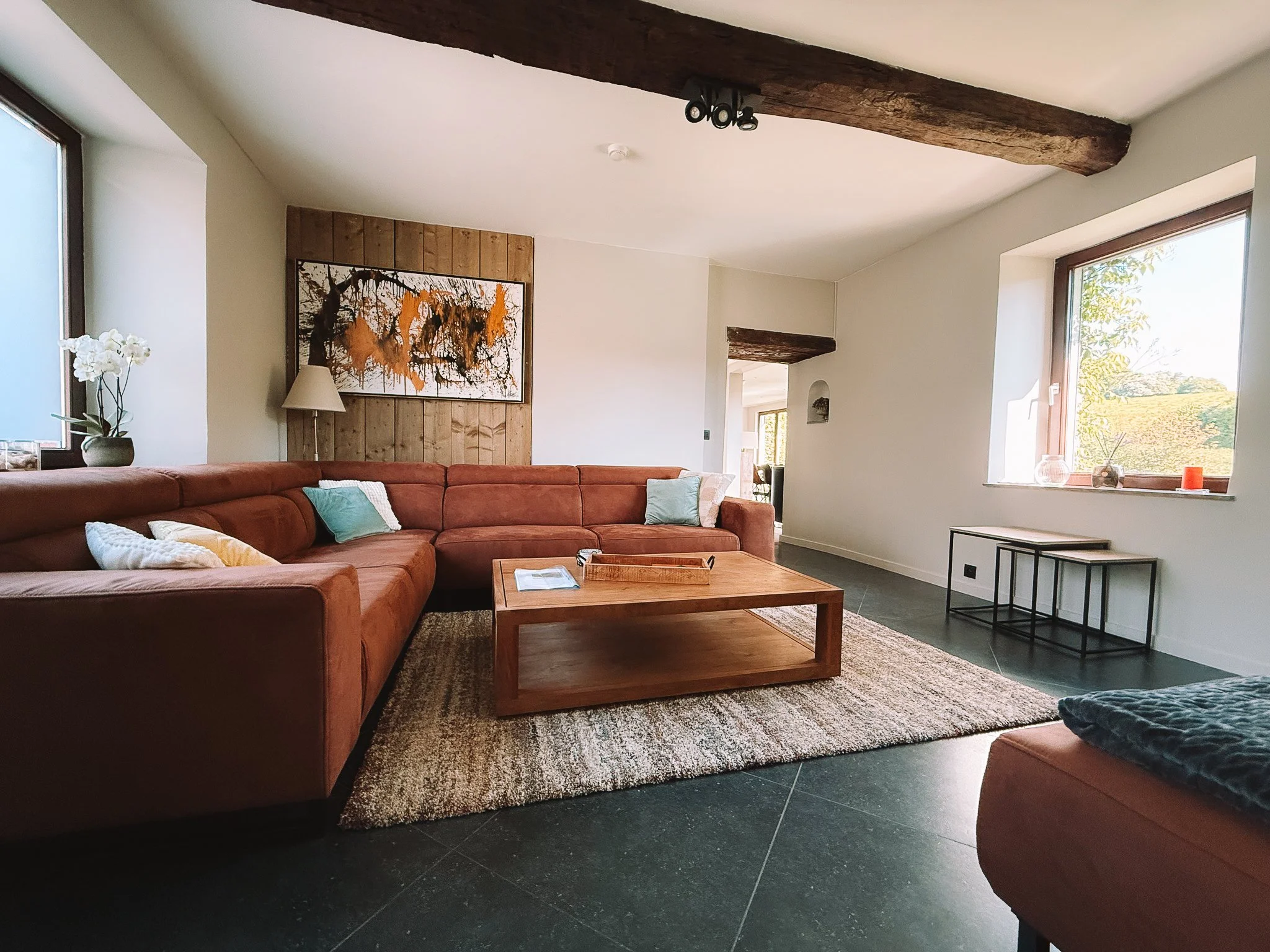 Woonkamer van het vakantiehuis Au bord du Floyon met grote hoekbank, groot raam, houten salontafel en gestreept vloerkleed.