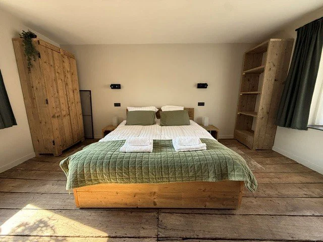 Een slaapkamer met vier stapelbedden van hout, twee aan elke zijde van het centraal gelegen raam met uitzicht op de bomen.