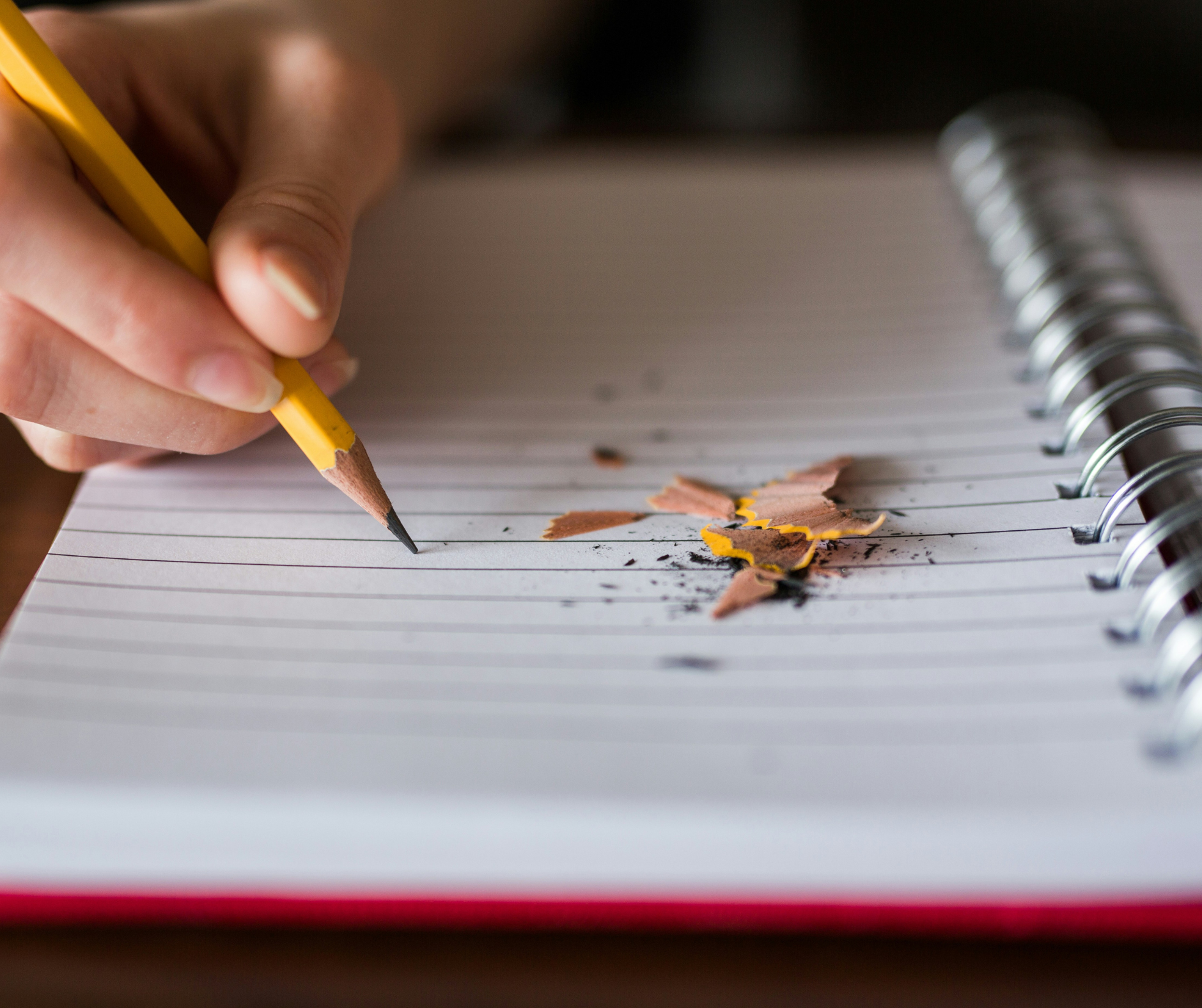 A student writes with a sharpened pencil in a notebook, working on essays and tasks related to college admissions counseling services.