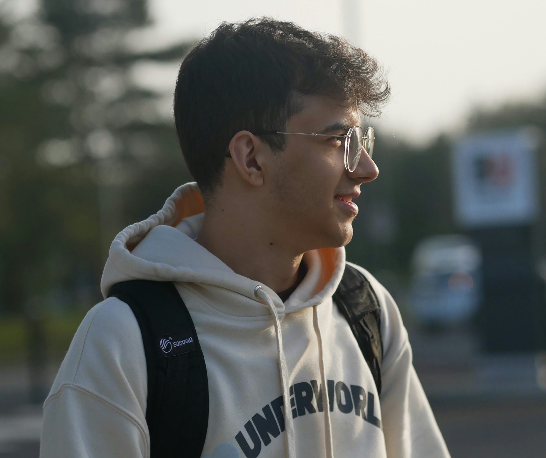 A student wearing glasses and a hoodie smiles while walking on campus, representing students guided by college admissions counseling support.