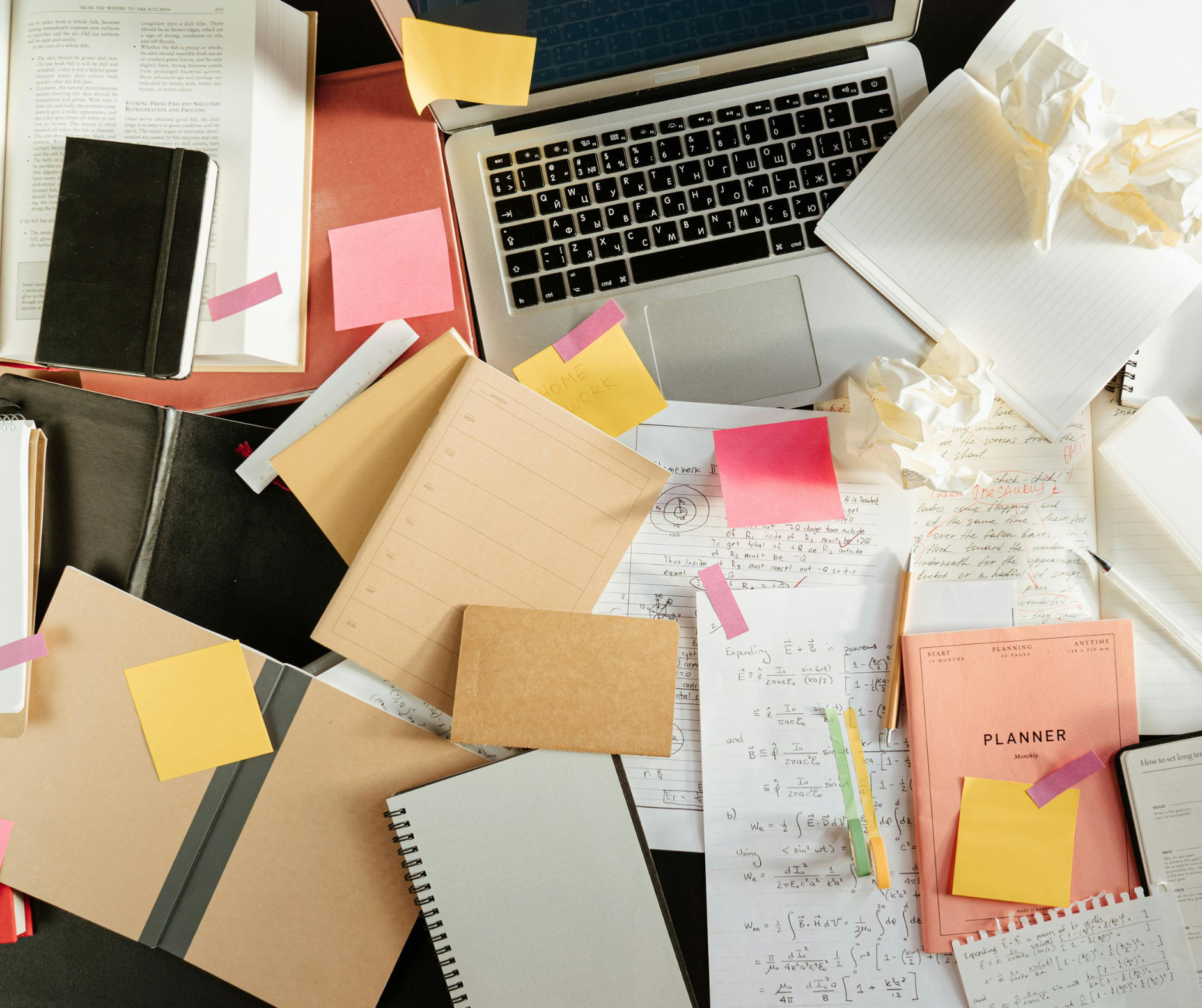 A cluttered study desk with notes, books, and a laptop, symbolizing the busy process of college admissions counseling and preparation.