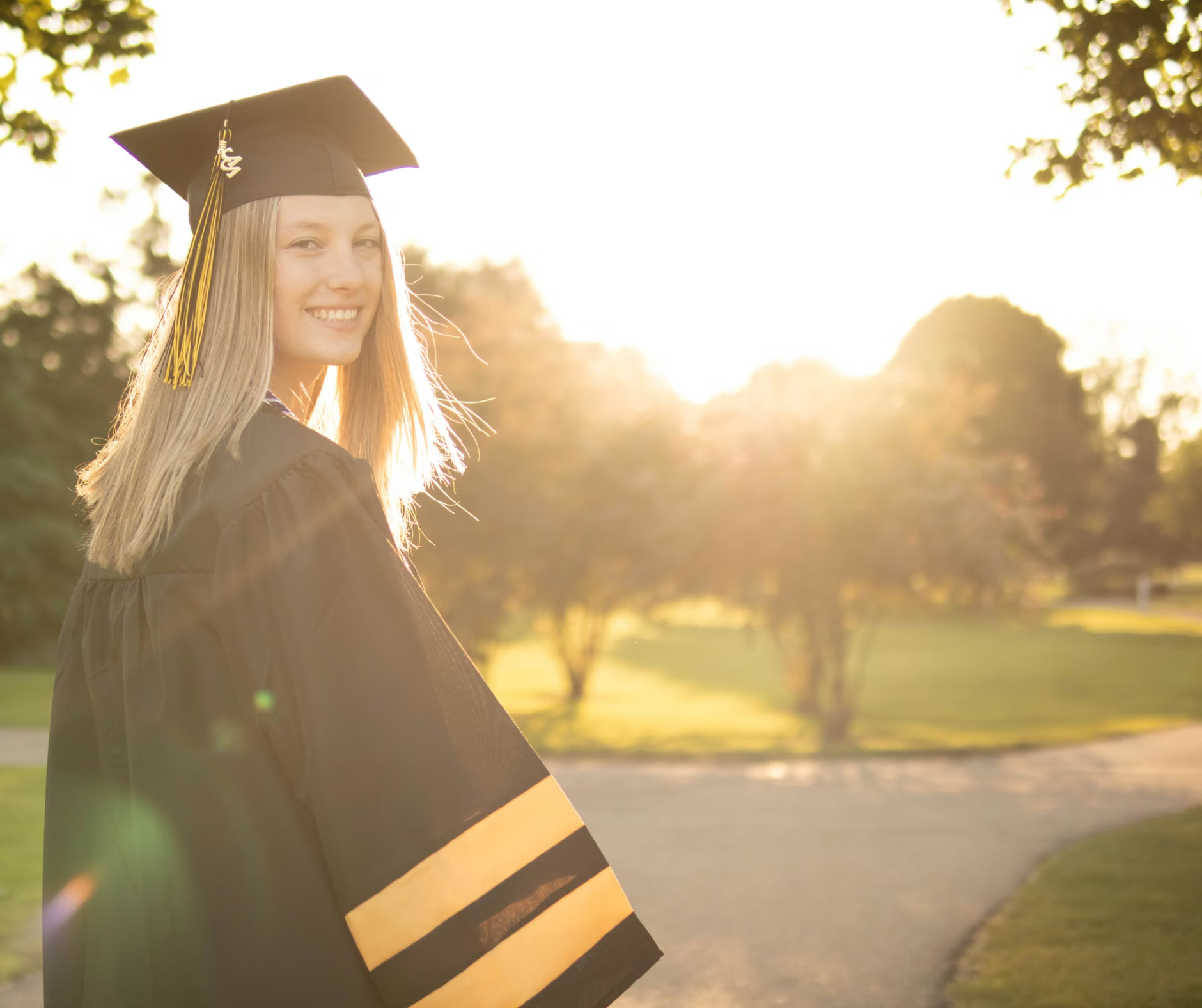 A graduate in cap and gown smiles in the sunset, symbolizing successful outcomes supported by college admissions counseling services.