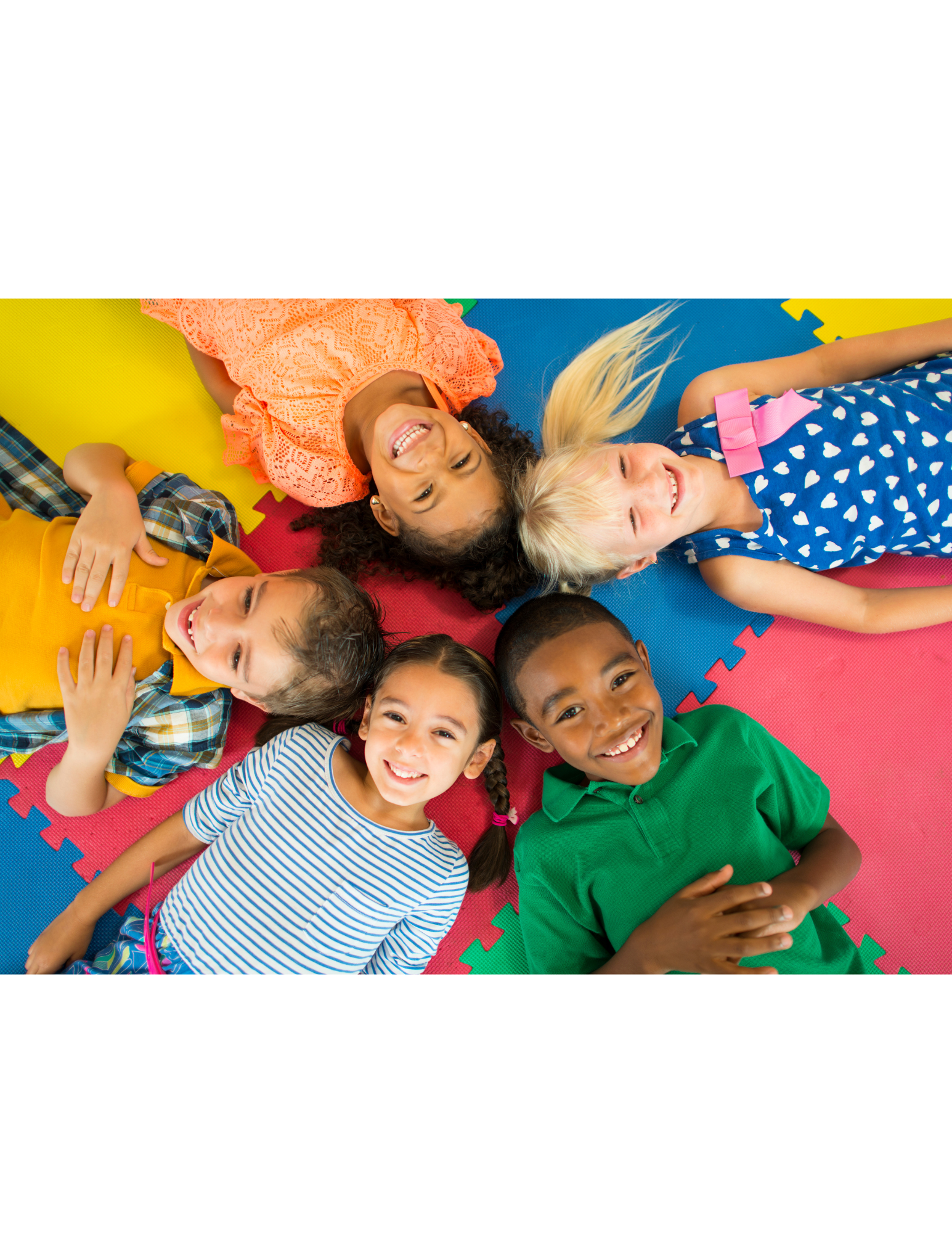 Group of six children lying on colorful foam puzzle mats, smiling and looking up at the camera.