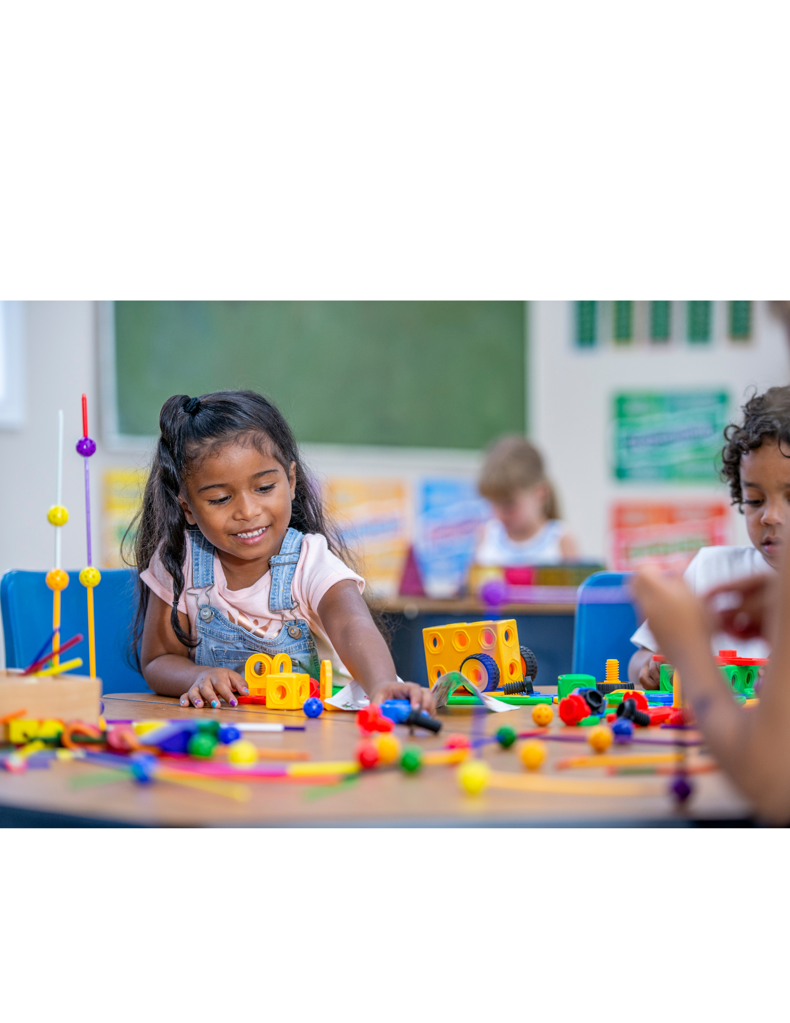 Young girl smiling and playing with colorful educational toys in a classroom.