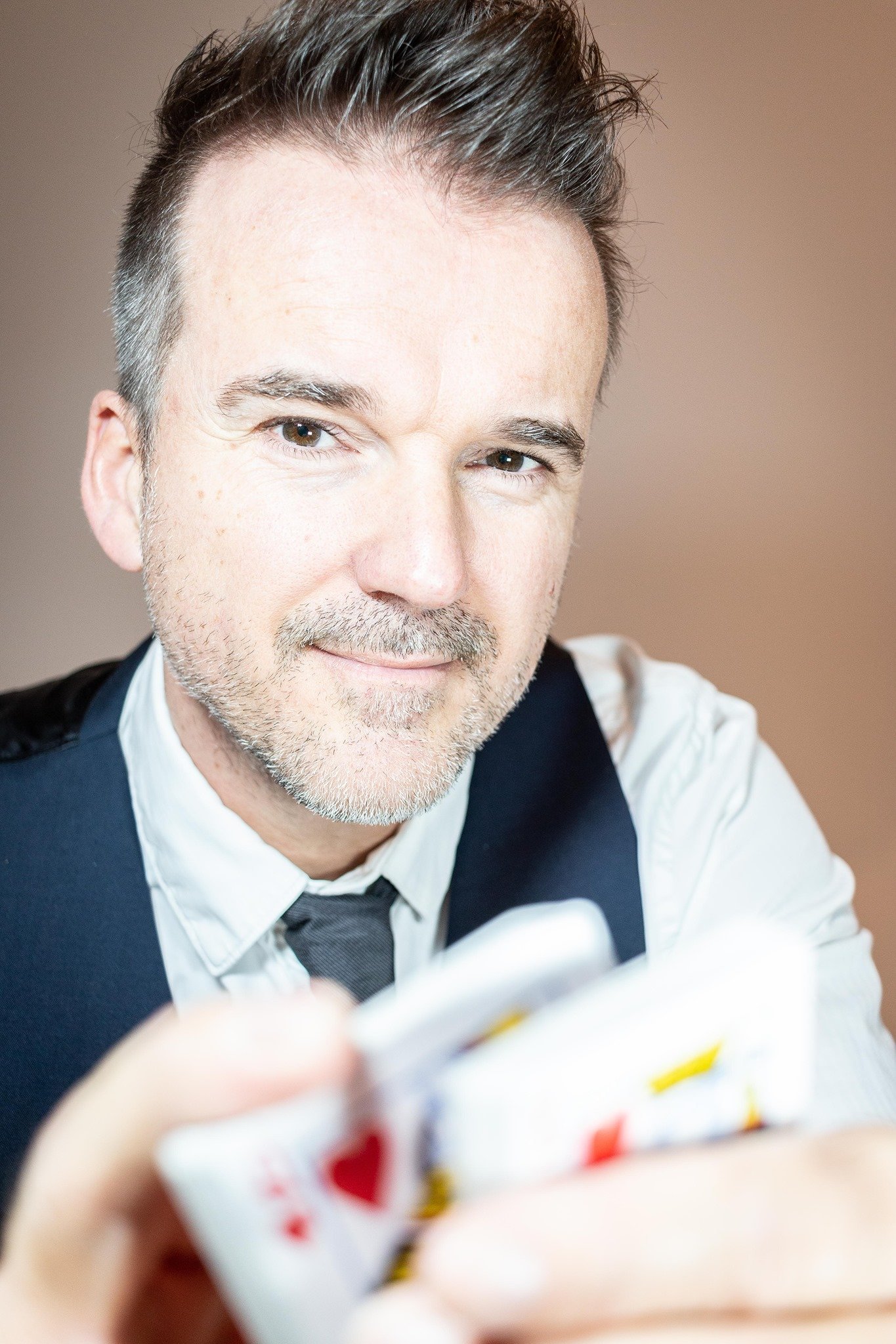 Nahaufnahme eines Mannes mit grauen Haaren und Bart, der Karten hält und einen freundlichen Blick zeigt.