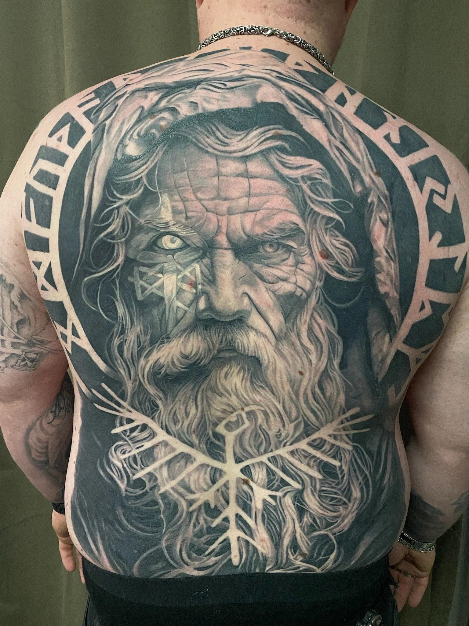 Lähikuva henkilöstä, jolla on suuri mustavalkoinen tatuointi, joka kuvaa Germaanista Jumaluutta Odin -zodia ja valkoista puun muotoista kuviointia. Näkyy myös rannekello ja sormus.