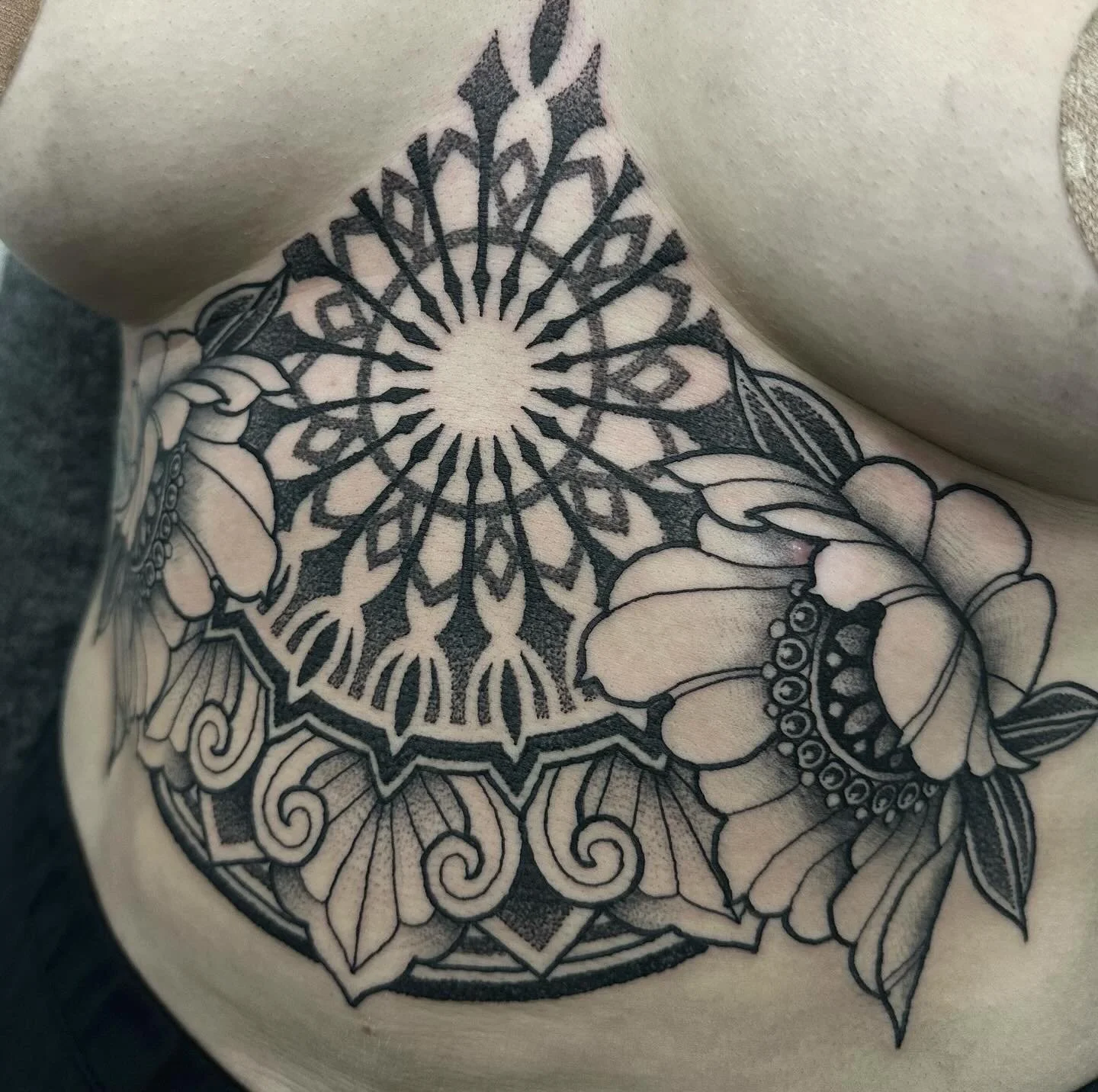 Mustekuva, jossa musta ja harmaa mandala-tyylinen tatuointi, jonka ympärillä on kukkia.