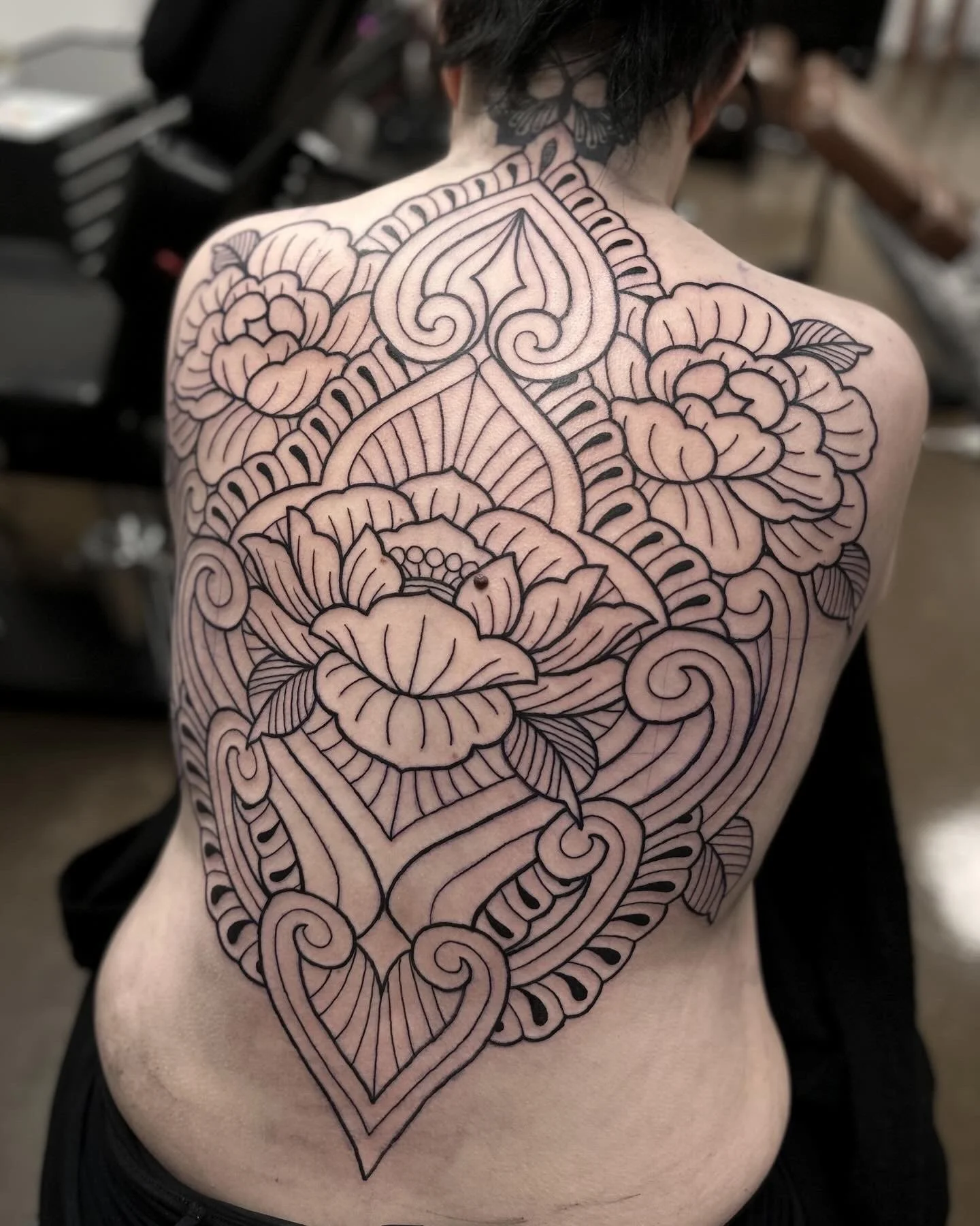 Henkilön selkä, jolta on tatuoitu suuret, yksityiskohtaiset mustat viivat ja ornamentit, mukaan lukien sydämen muoto ja kukkia.