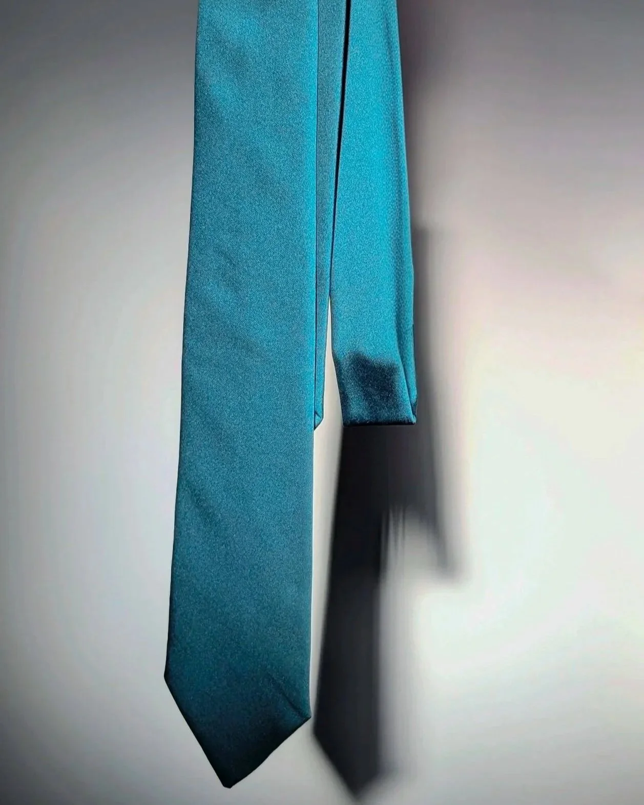 A teal tie hanging in front of a white background