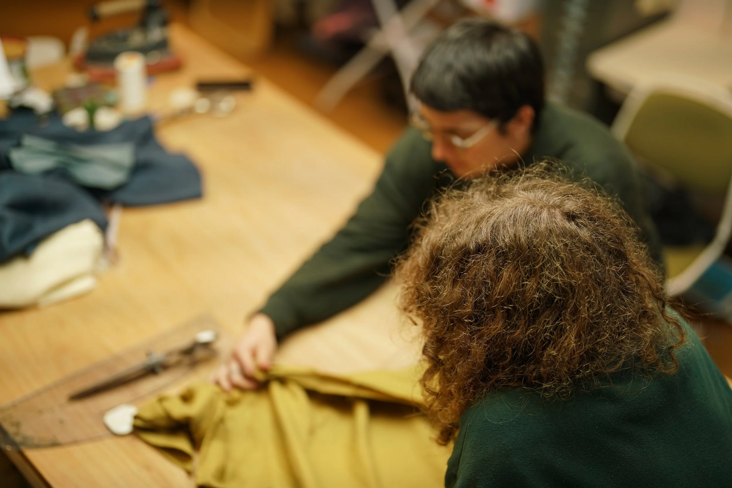 Two people working together on a sewing project, with fabric and tools on a wooden table.