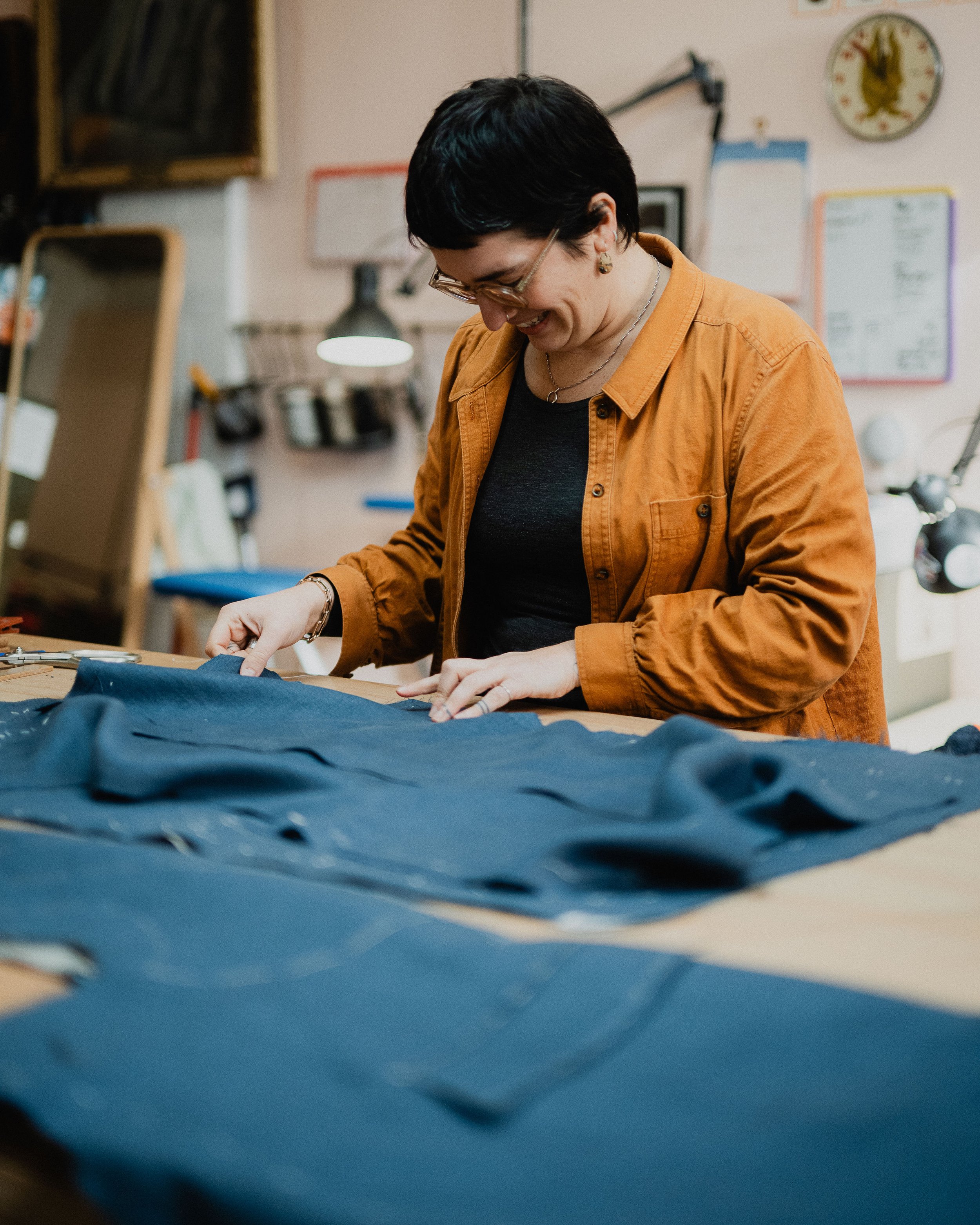 A woman with short dark hair and glasses working on a blue piece of fabric in a workshop.