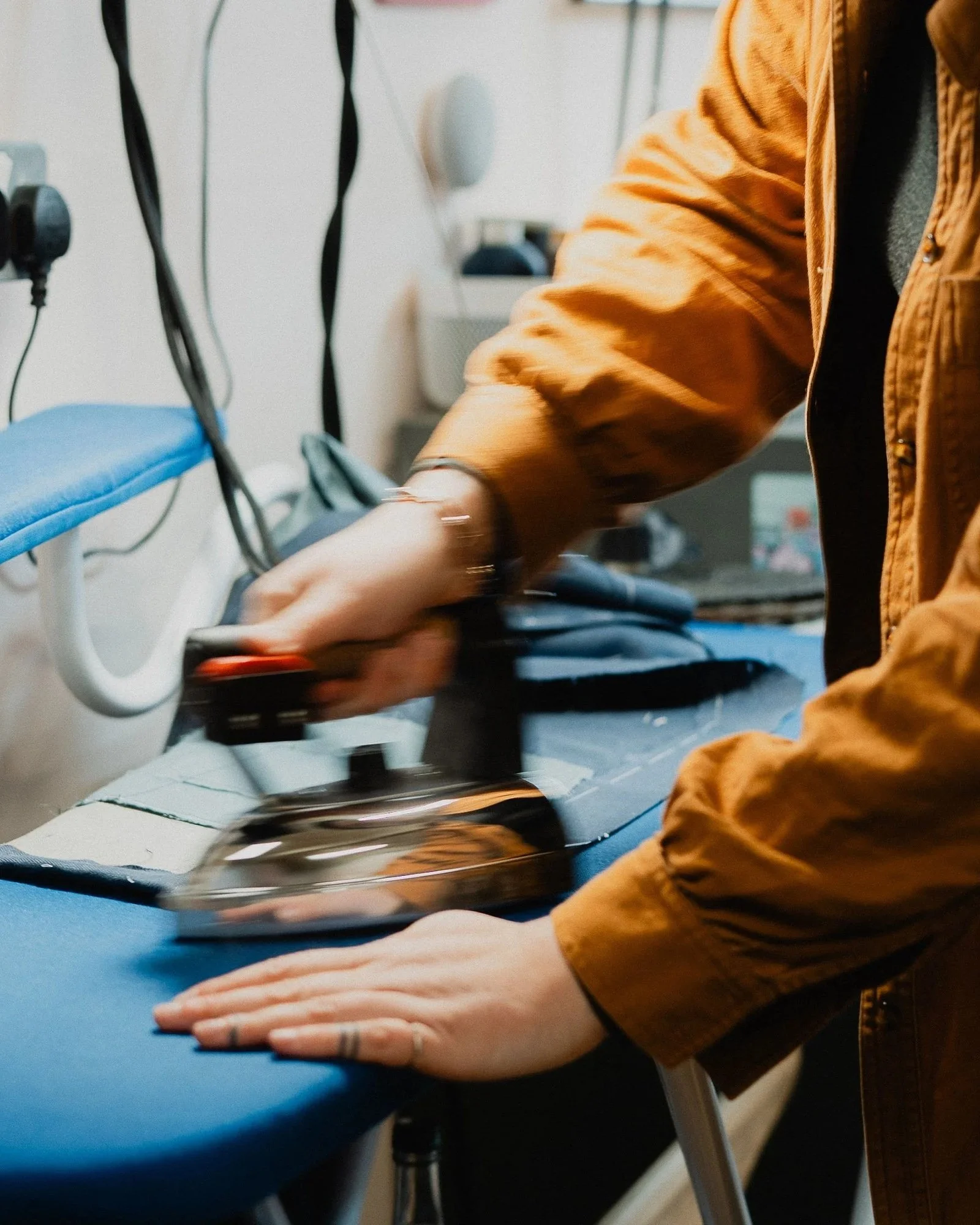 close up of an iron in motion as a woman in an orange shirt presses something on a blue ironing board