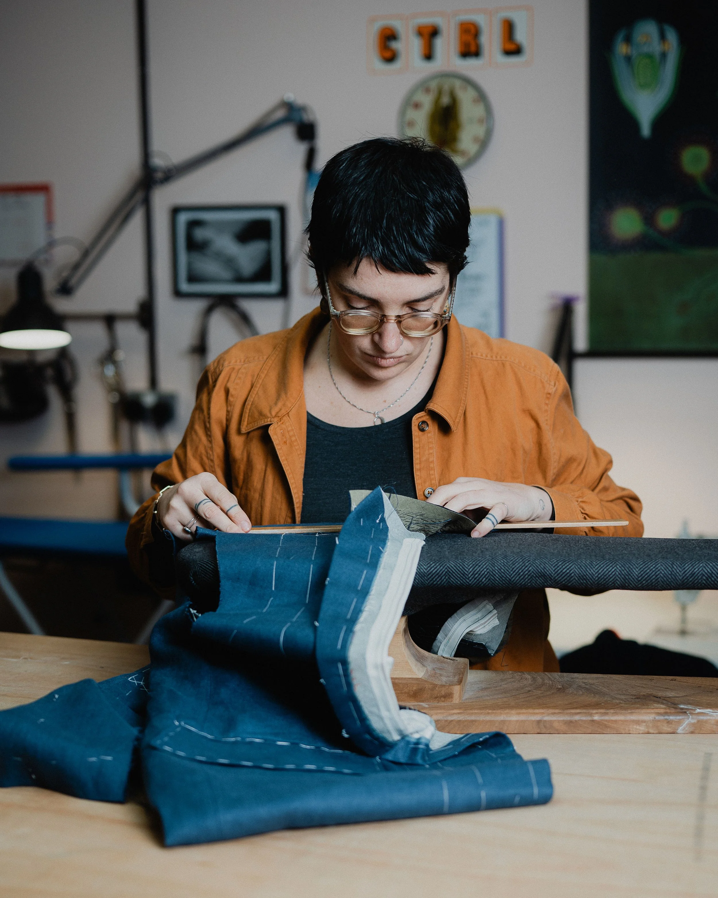 Person sewing or tailoring fabric on a worktable in a workshop.
