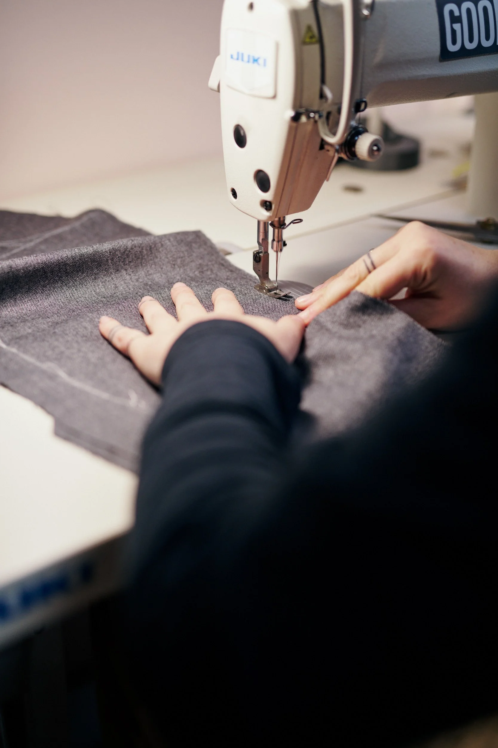 Person sewing dark gray fabric using industrial sewing machine.