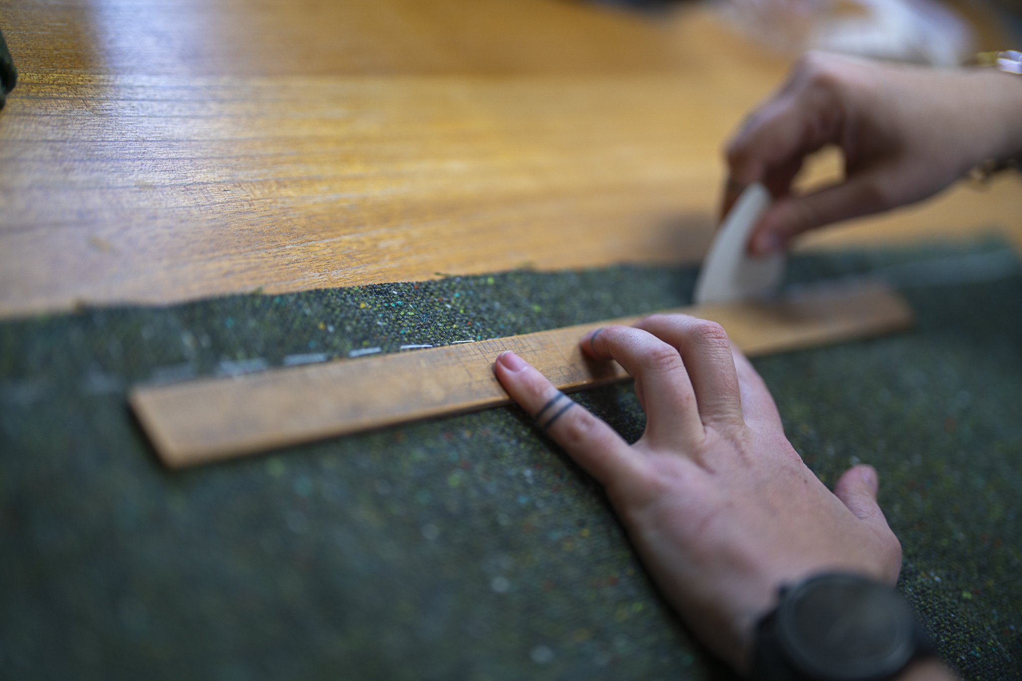 Hands using a ruler and tailor's chalk to mark fabric on a wooden table.