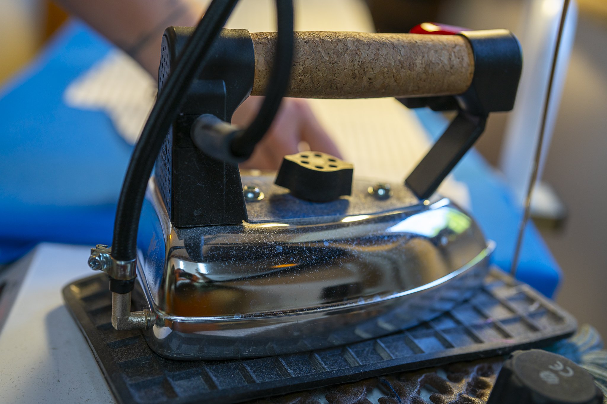Close-up of a vintage steam iron with a cork handle, resting on a heat-resistant pad.
