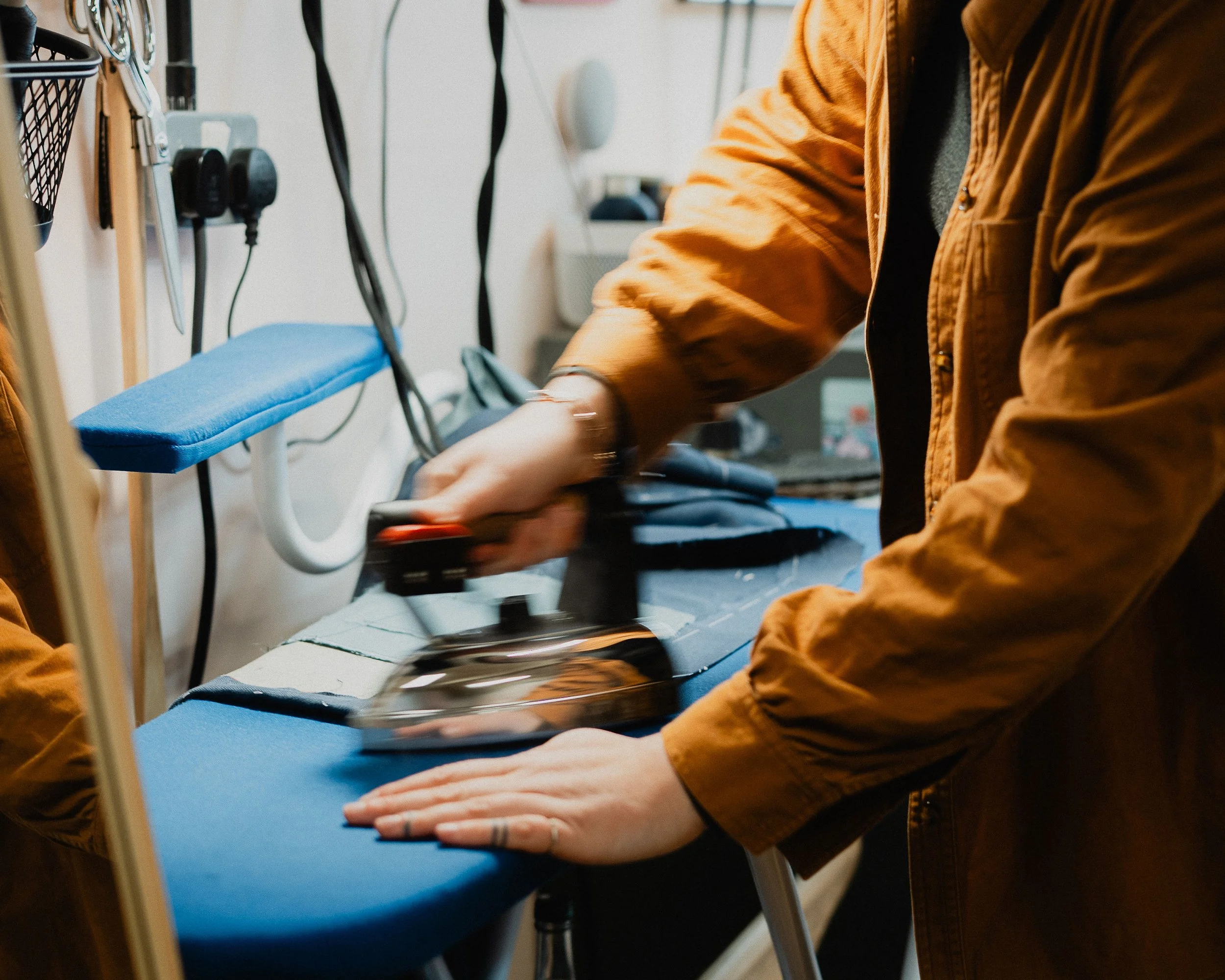 Person in a brown jacket using an iron on a piece of fabric on an ironing board.