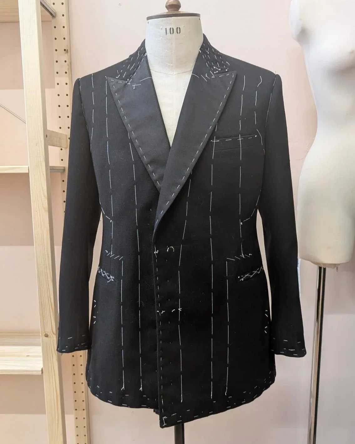 Black suit jacket on mannequin with visible white outlining markings for tailoring.