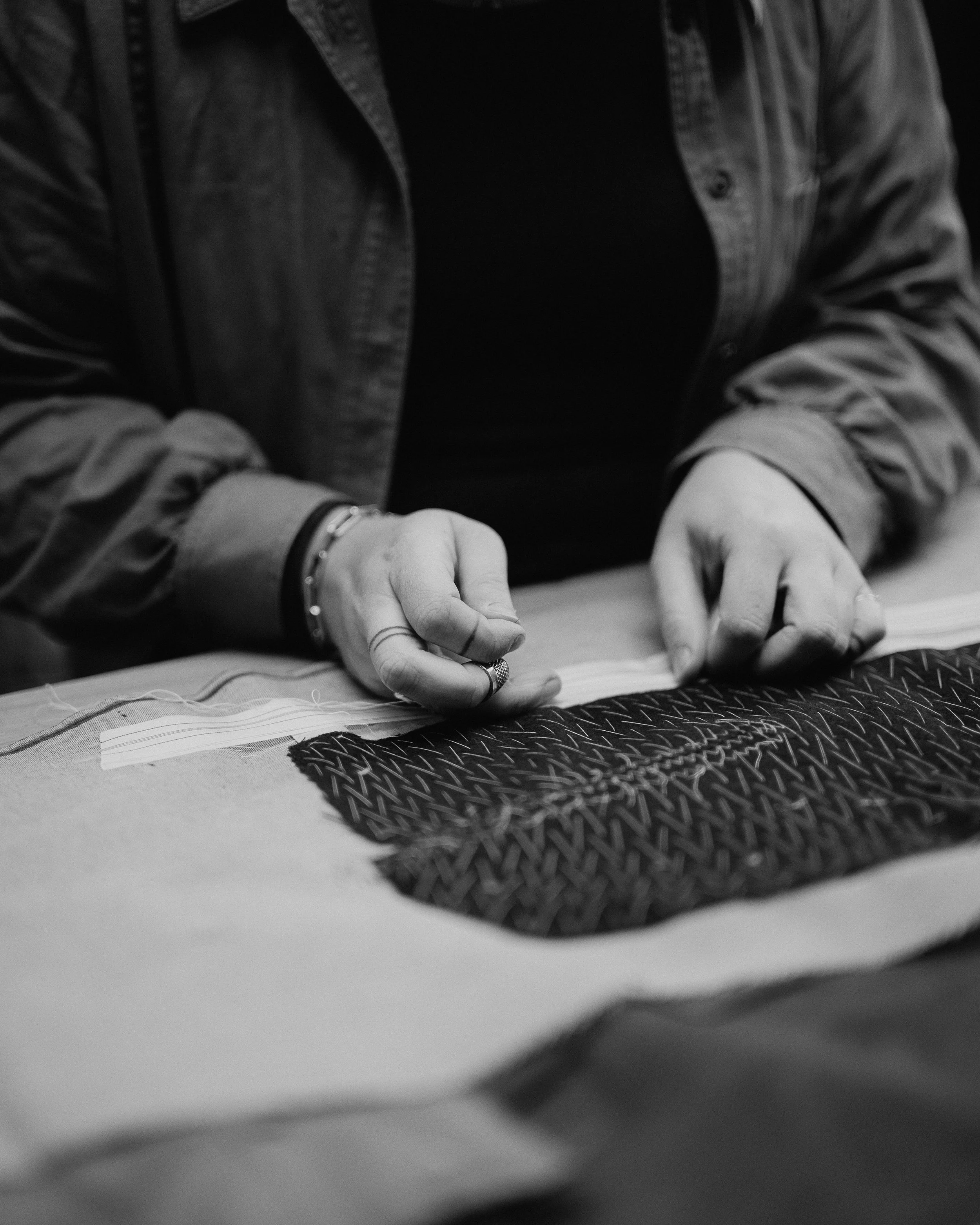 Person working on textile or fabric, manipulating a woven pattern on a table in black and white.