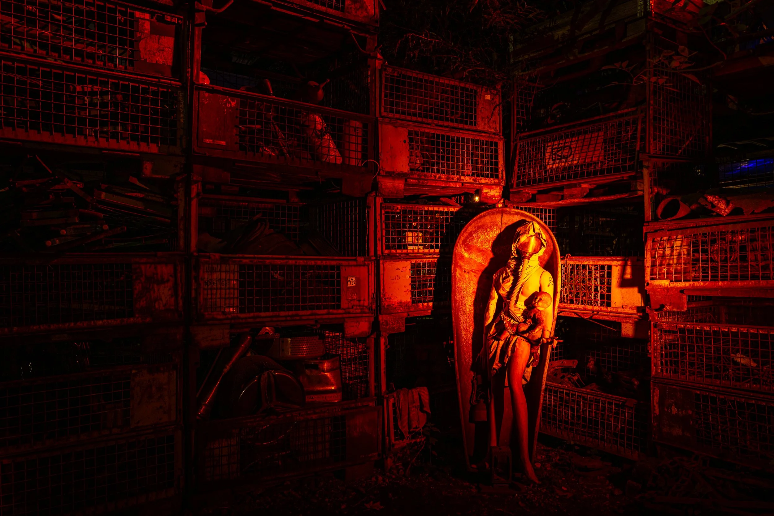 A horror movie set with a dim red lighting, displaying a horror-themed statue of a mother holding a baby, surrounded by metal cages and old tools.