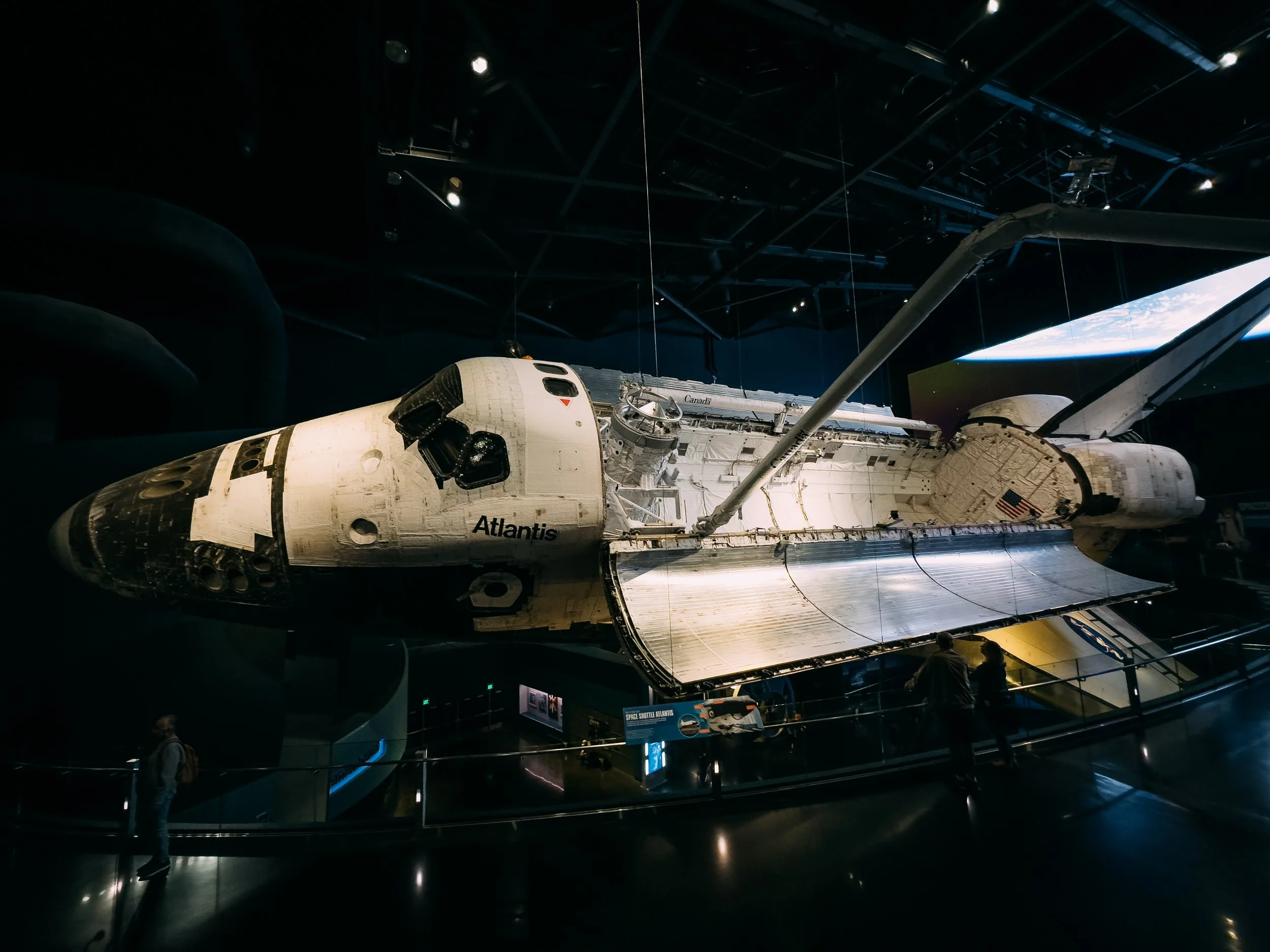 Space shuttle Atlantis displayed inside a museum, with visitors observing.