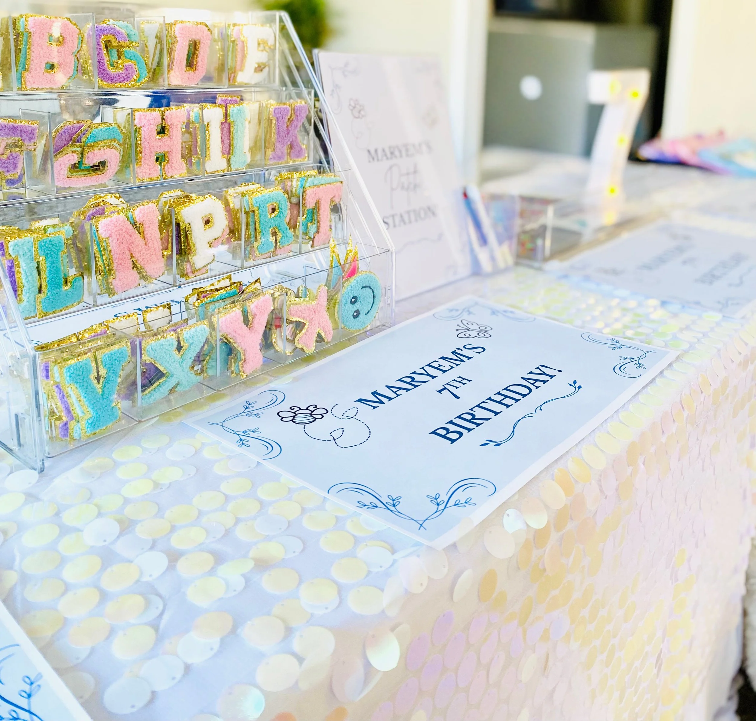 Decorative birthday party table with colorful cake cookies spelling 'HAPPY BIRTHDAY' and a sign that says 'Marven's 4th Birthday' on a pastel-colored tablecloth.