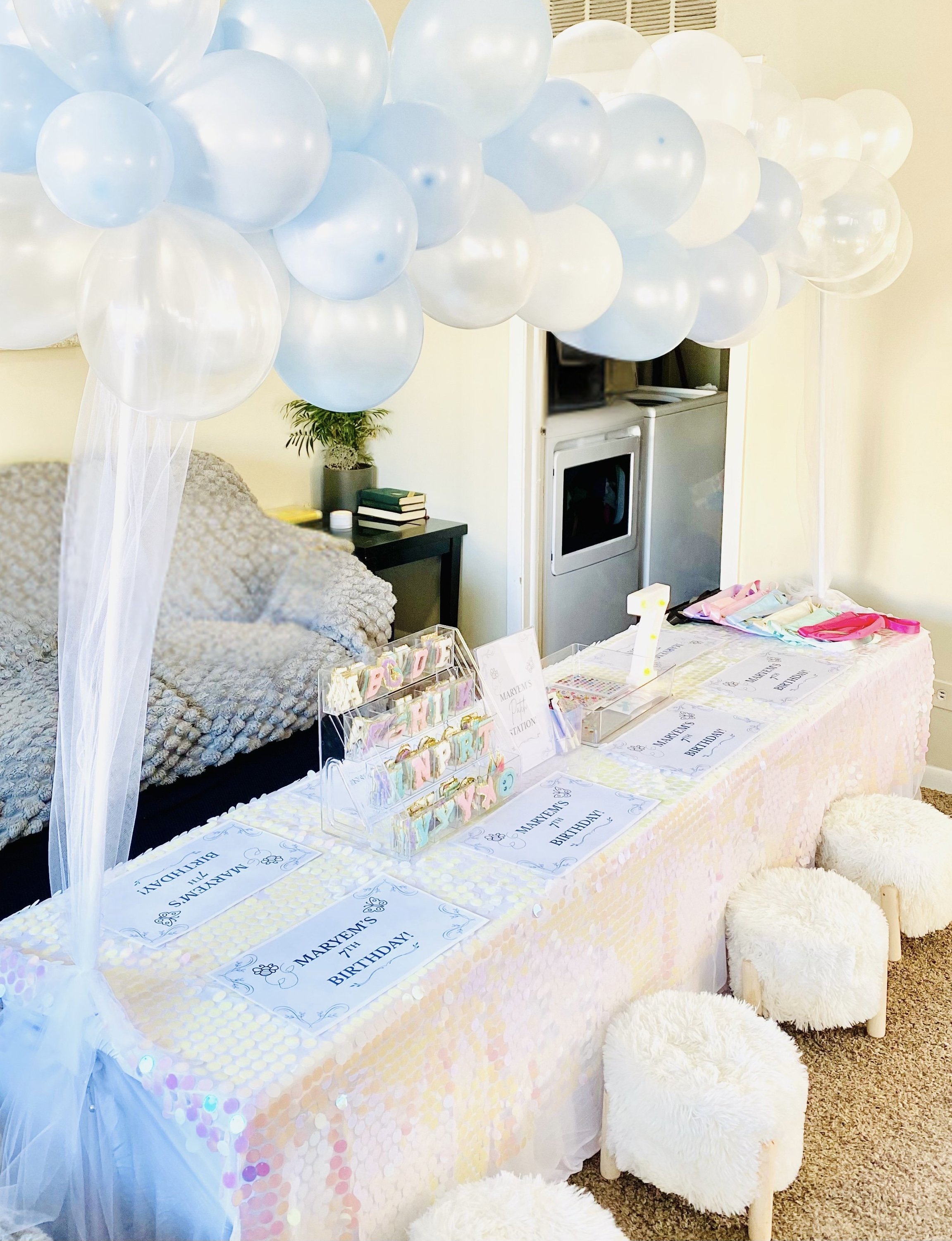 Decorated birthday party table with pastel-colored balloons, signs, and small stools with furry covers.