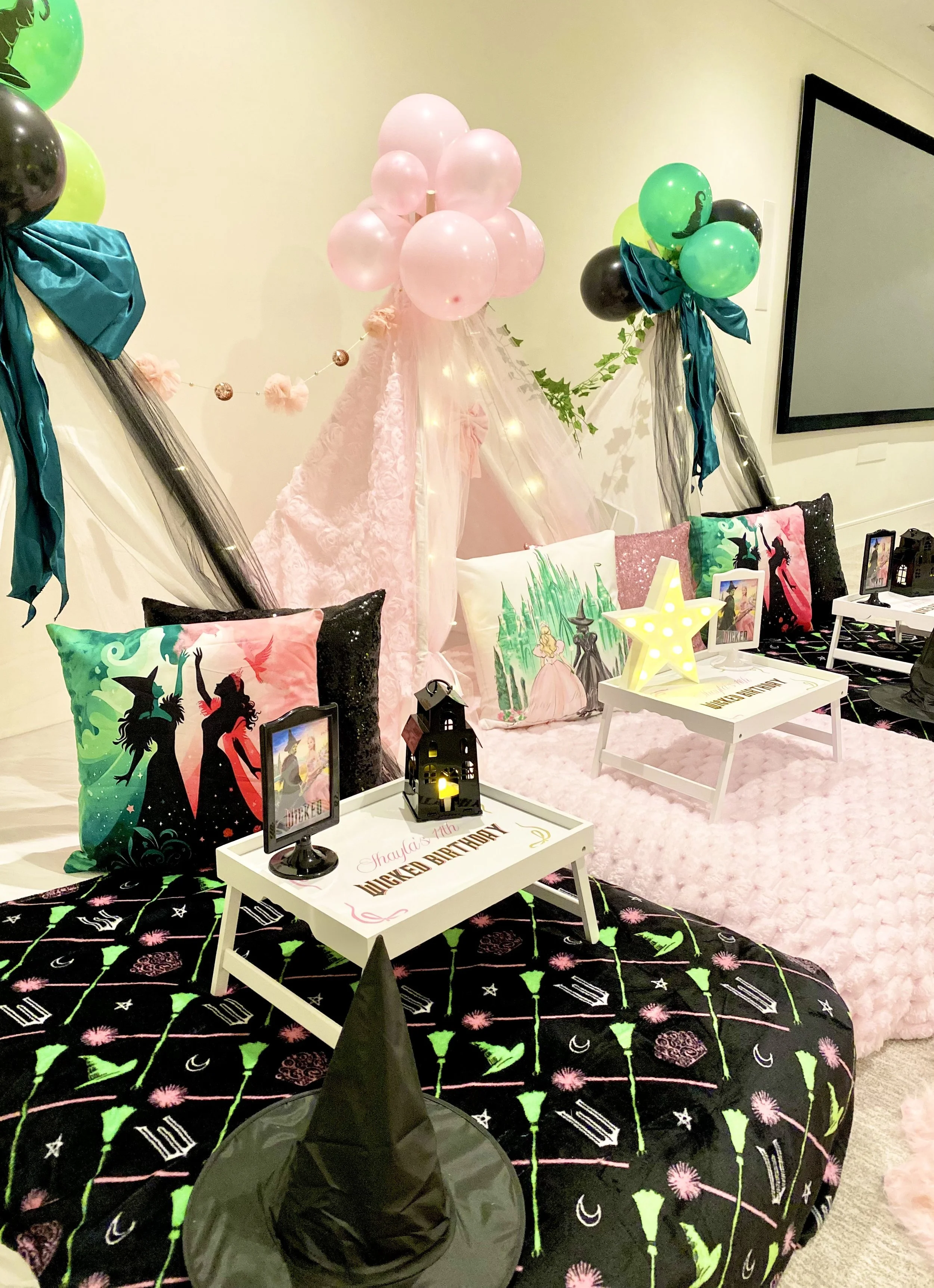 Decorative setup for a birthday party with a Harry Potter theme, featuring a pink canopy, lanterns, pillows with Harry Potter characters, balloons, and themed table decor.