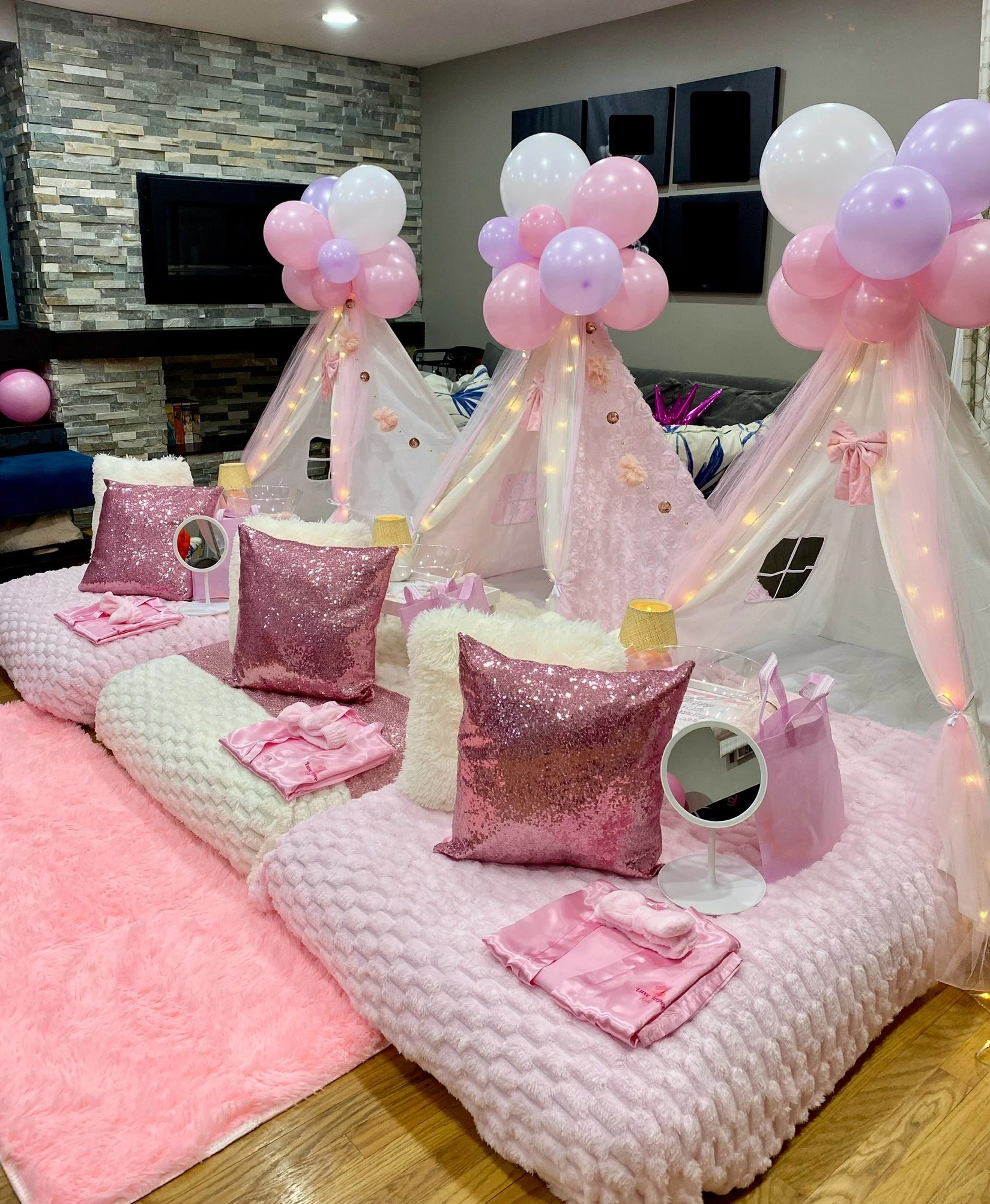 A pink-themed, decorated room for a children's gathering or party with cushions, balloons, small tables, and makeup or craft items.