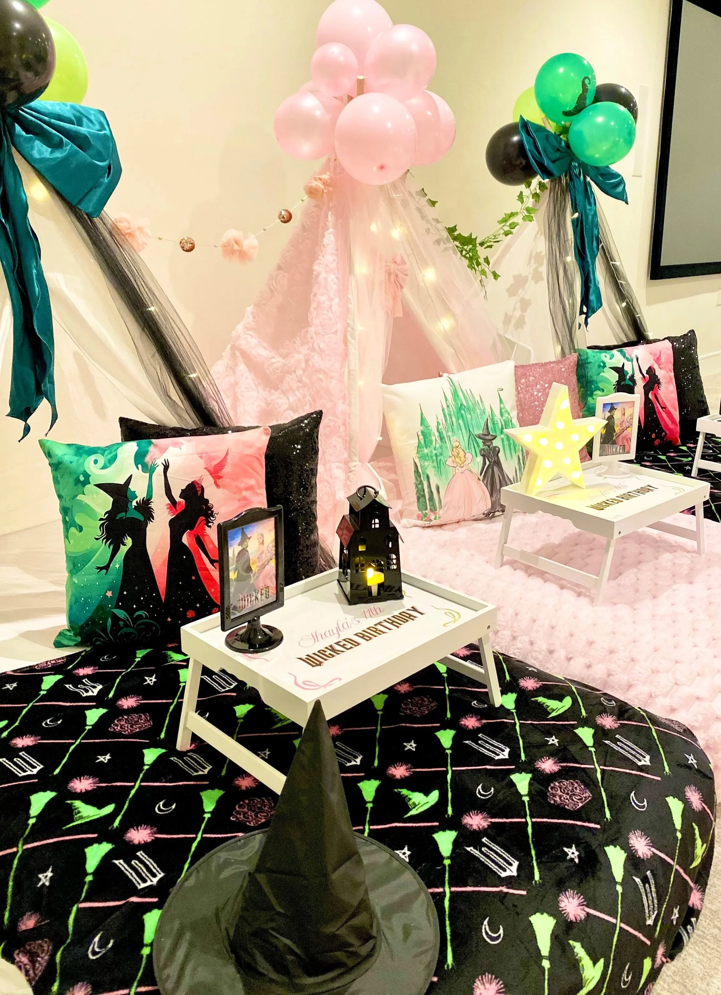 Fairy-themed birthday party setup with fairy tale pillows, a pink teepee tent decorated with pink balloons, and a wizard hat on a table.