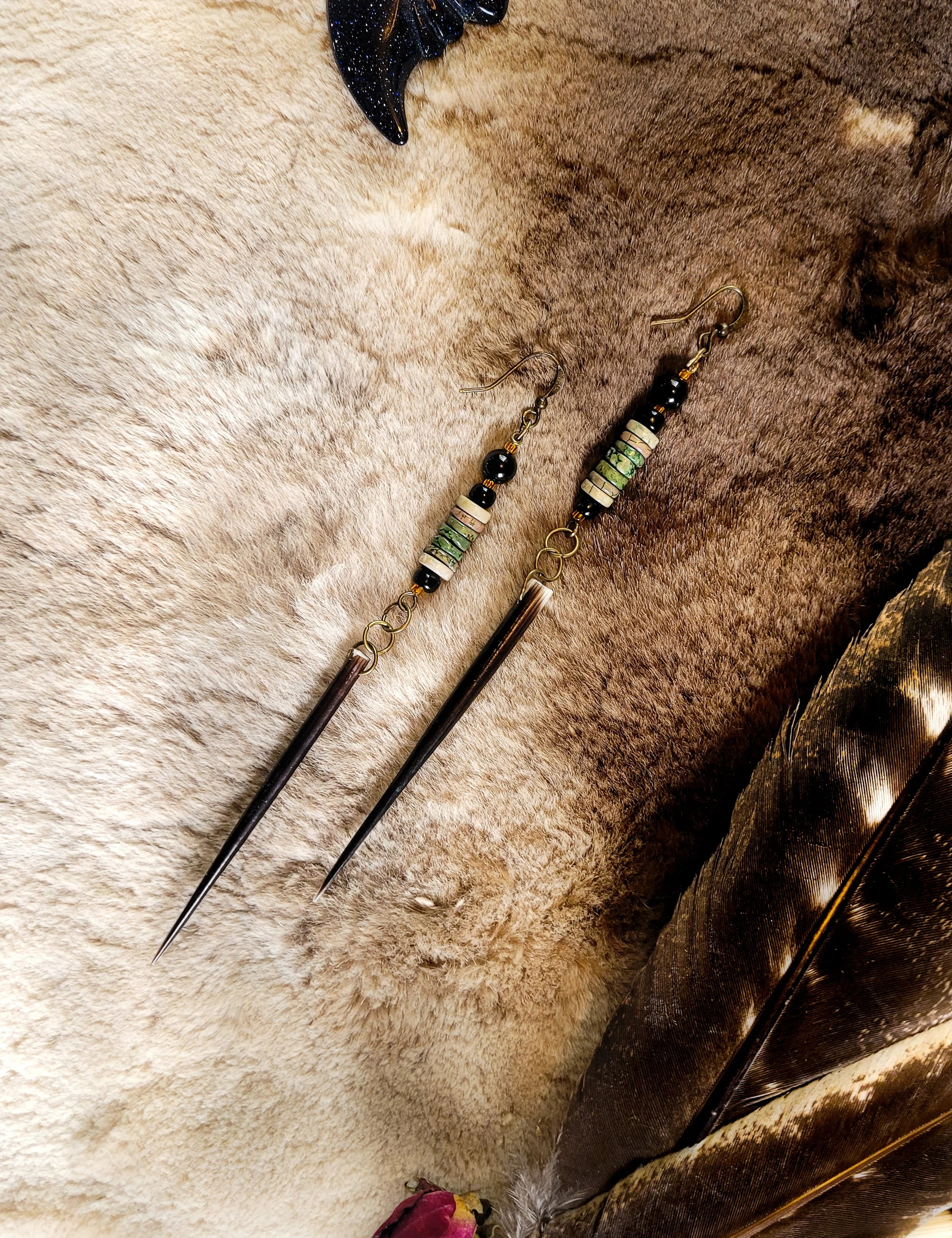 Photo of medium length, lightweight  African Porcupine Quill earrings displayed on light-to-medium dark brown fur next to feathers and  crystals. Earrings contain two long  brown, sharply tipped African porcupine quills, picture Jasper beads, tourmal