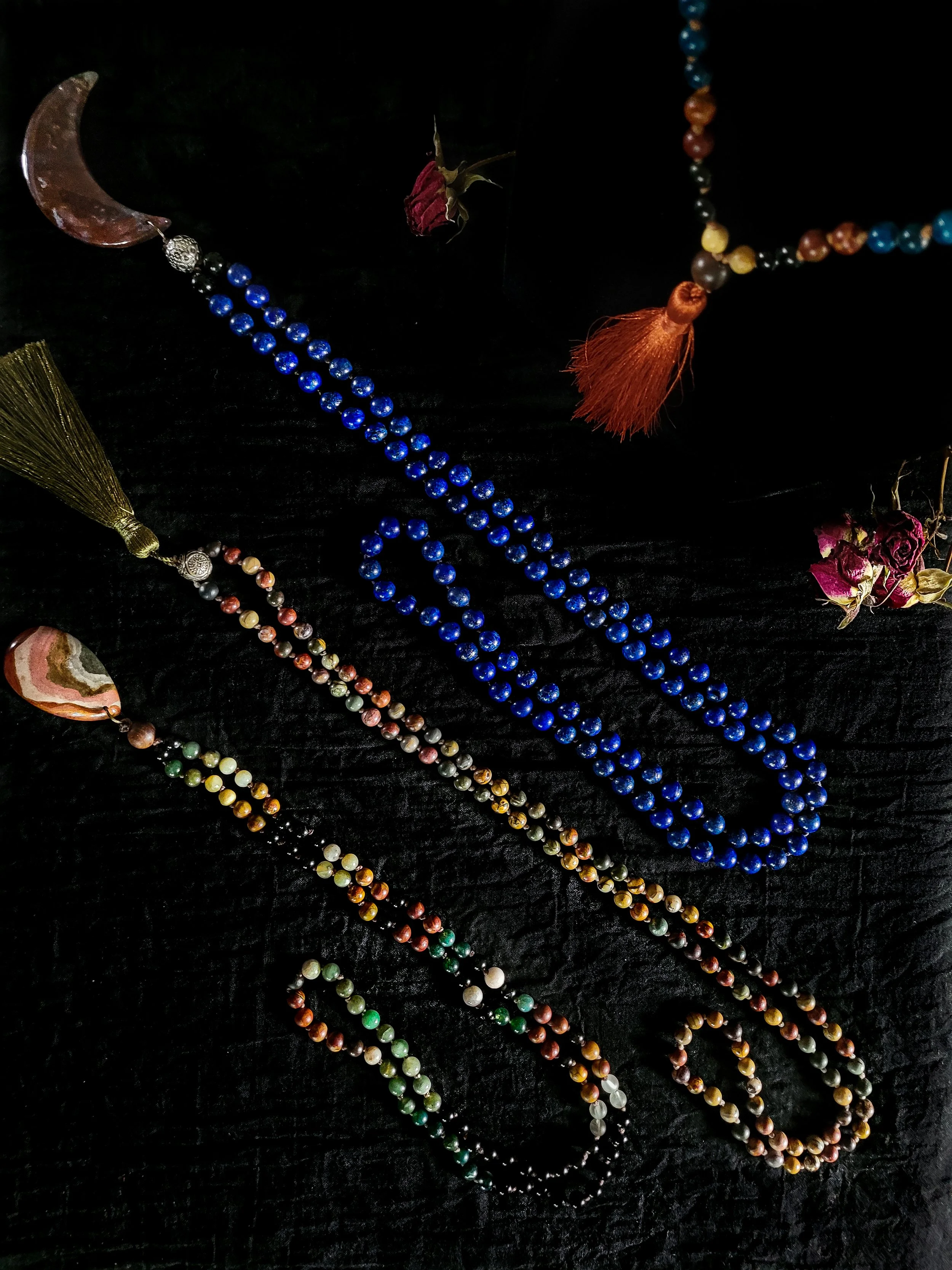 Photo of four custom-made limited gemstone mala necklaces with 8mm and 6mm beads; polychrome jasper and agate gemstone pendants; and a dark orange and an olive green silk tassel. Beads include dark blue lapis lazuli, green and yellow jade, amazonite,