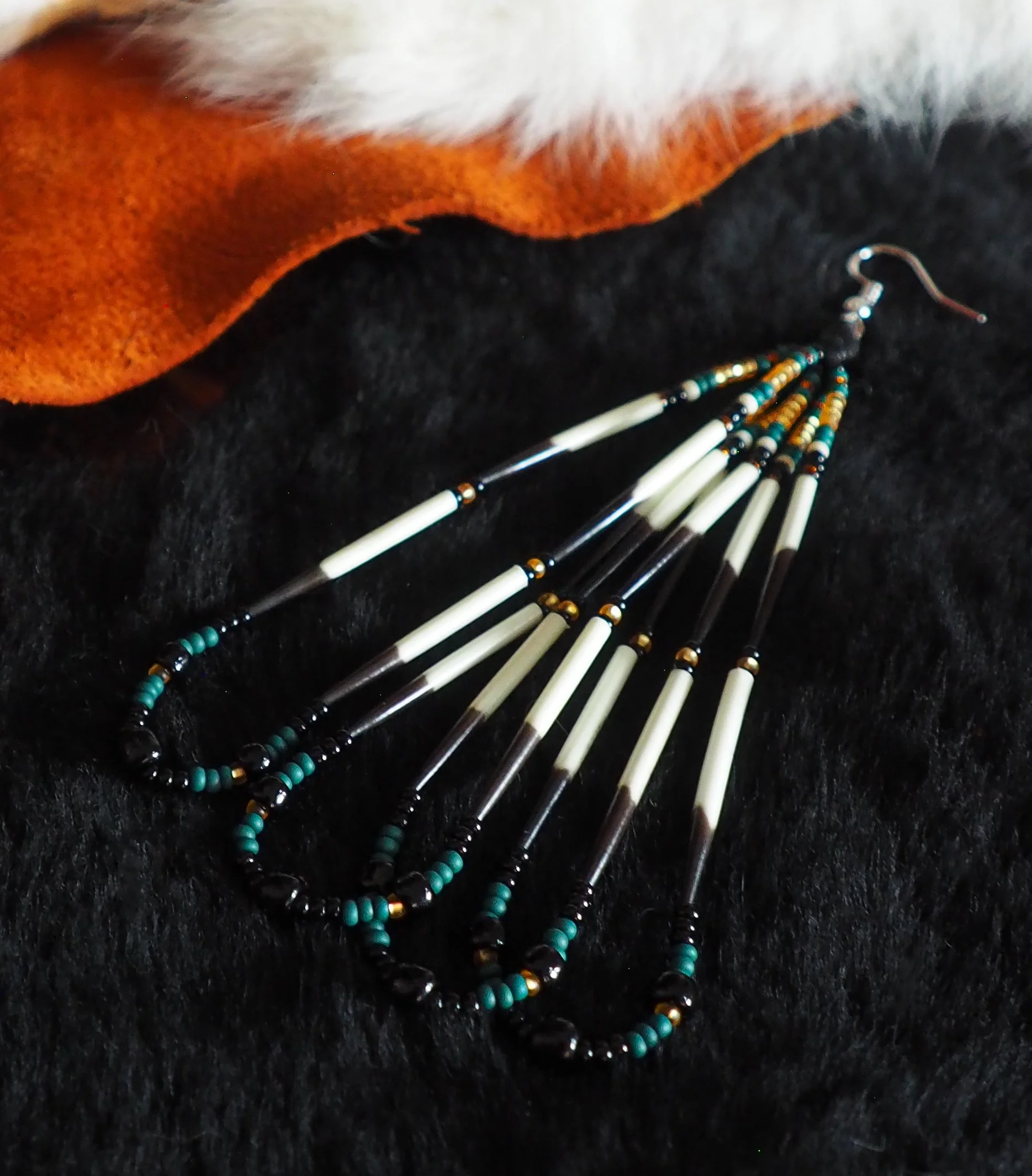 Photo of  large, lightweight traditional Ancestral Porcupine Quill earring laying on top of black fur, next to tan leather and white fur. backdrop. Medium length earring contains four looped segments in two tiers of 16 mostly white porcupine quills &