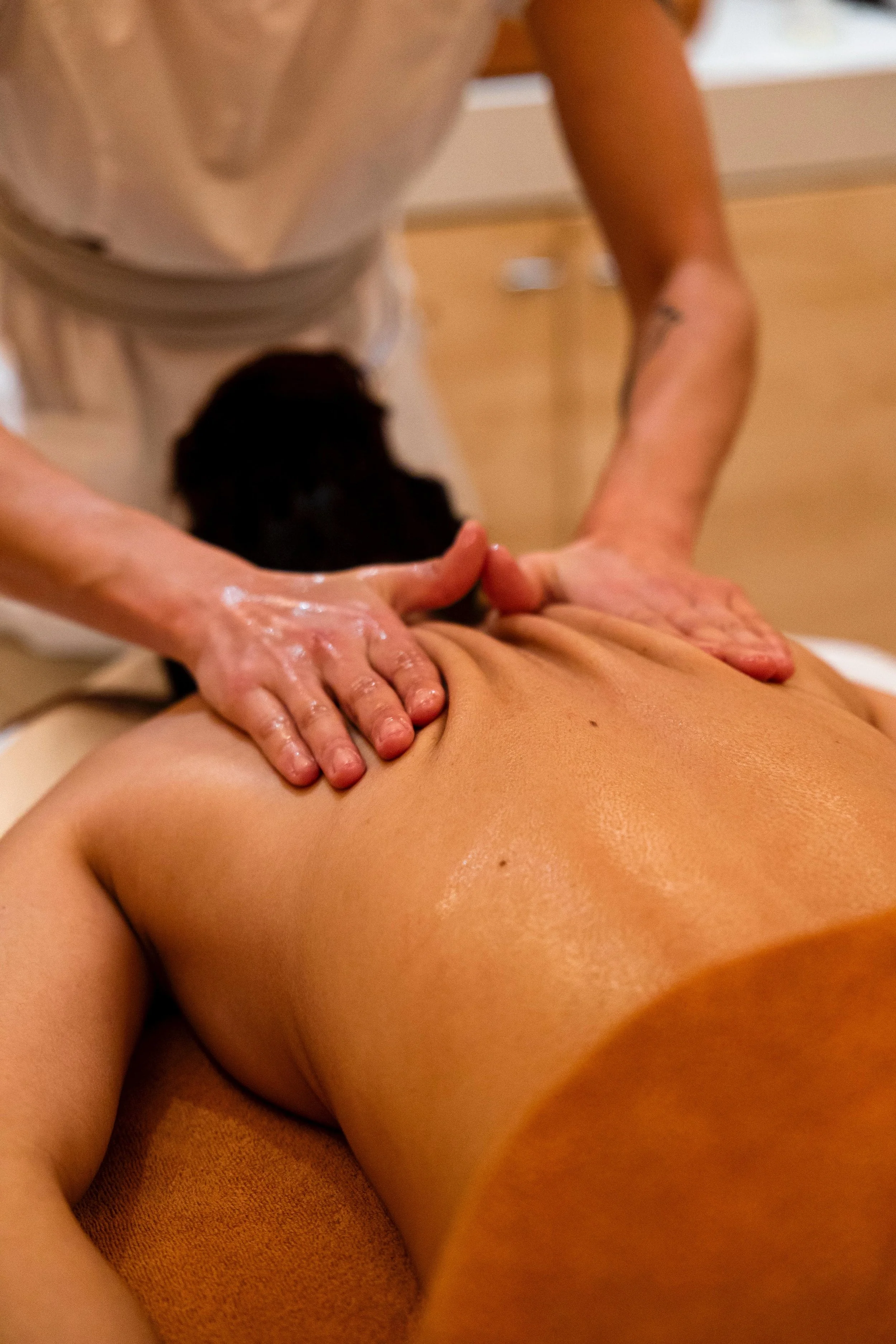A person receiving a back massage, lying face down on a massage table while a massage therapist applies pressure with their hands.