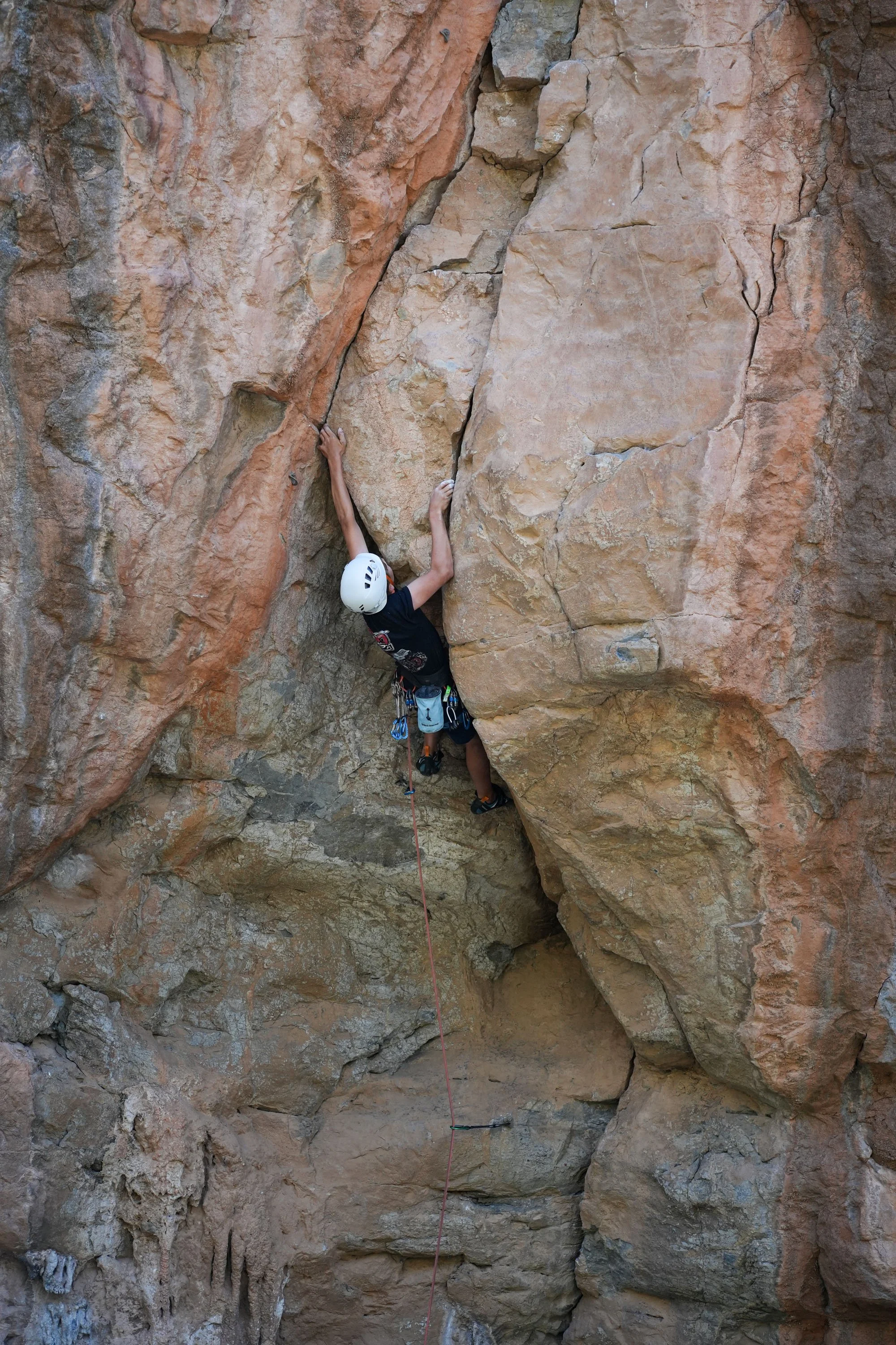 A person wearing a helmet climbing a rocky outdoor cliff, using safety ropes and harness.