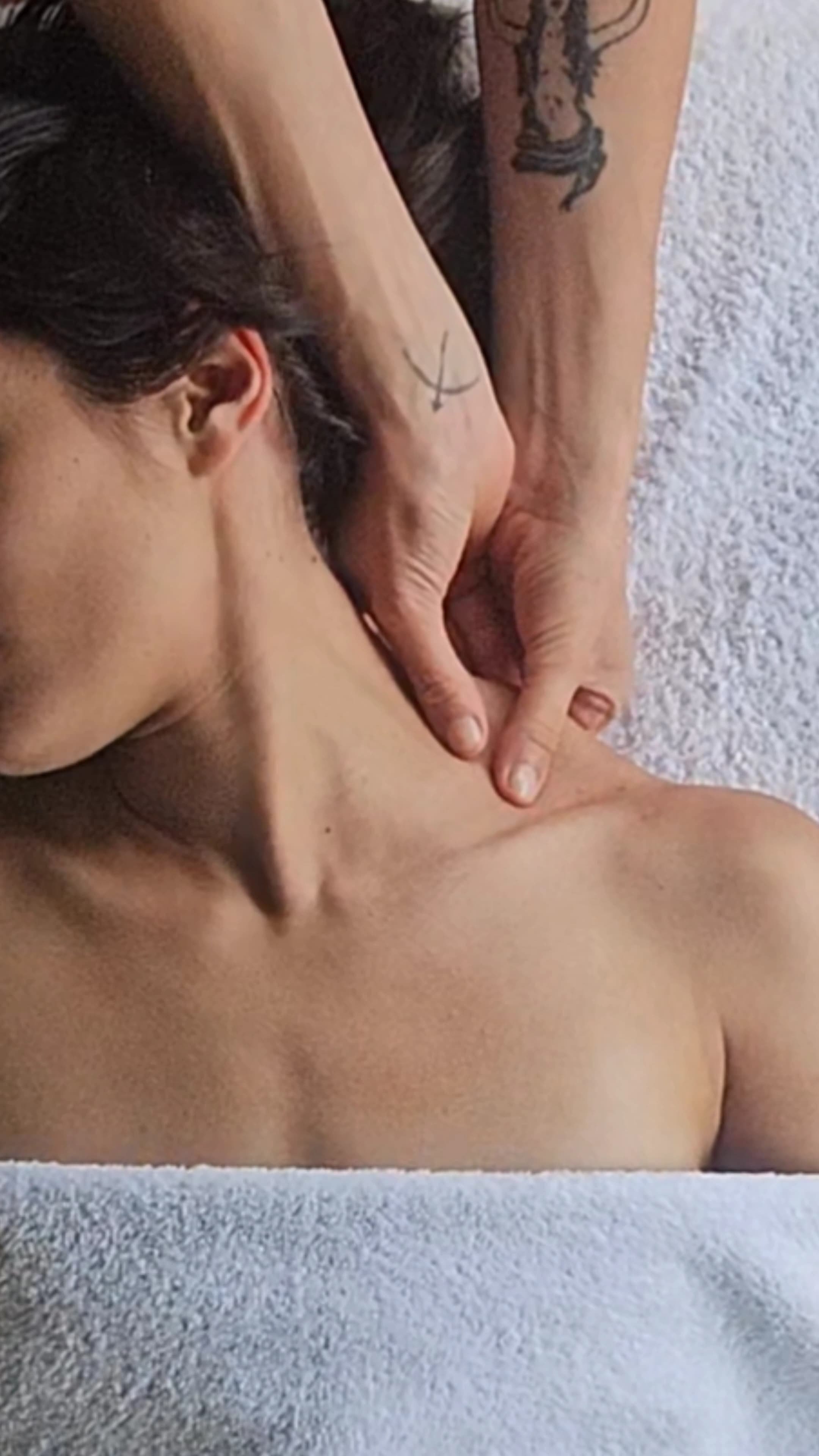 A person receiving a shoulder massage, lying face down on a towel, with their head turned to the side.