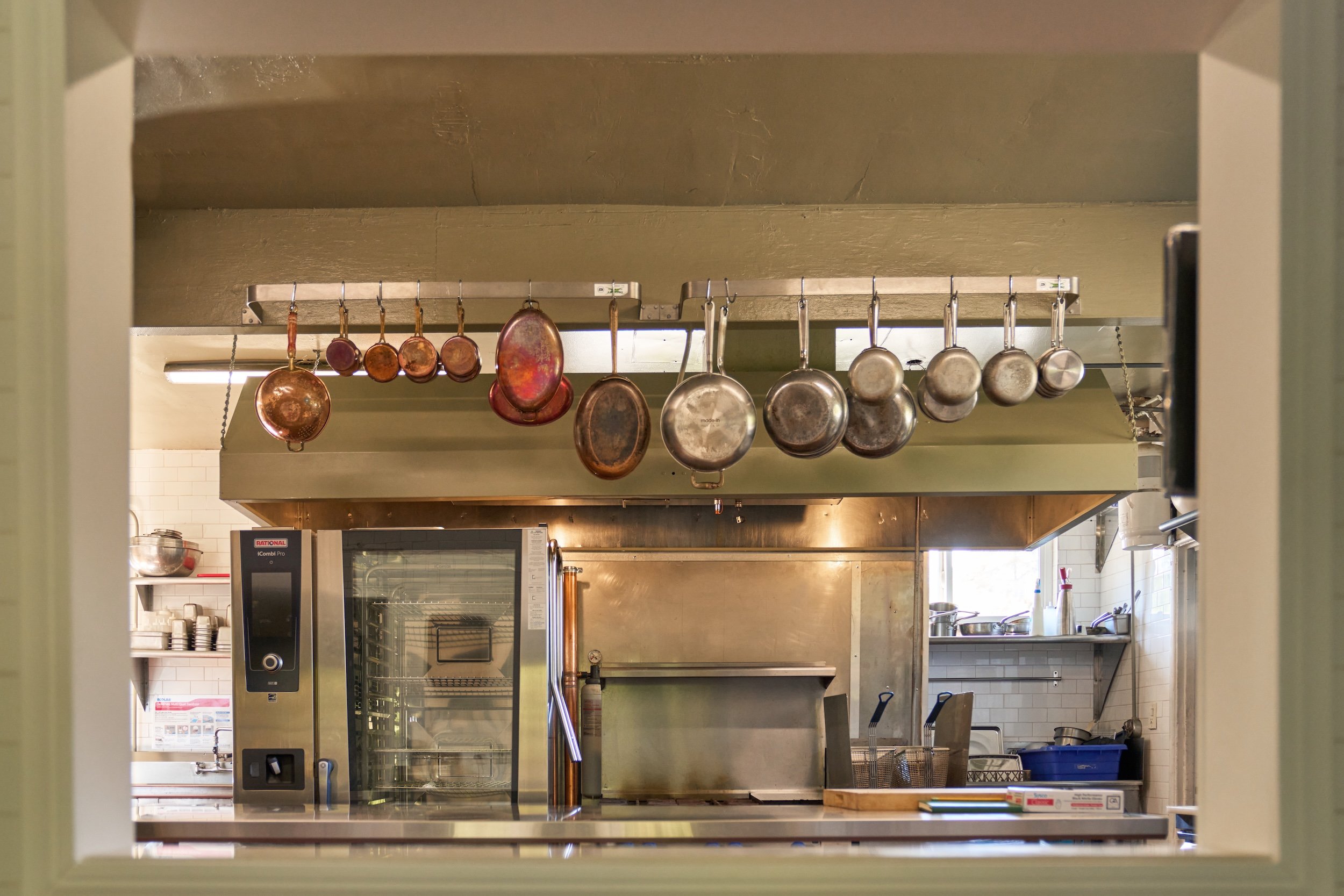 The window between our terrace and kitchen frames more than a view — it’s a quiet conversation. Guests catch a fleeting glimpse of the rhythm behind the meal, while the kitchen looks out onto rustling leaves, blooming herbs, and light filtering throu
