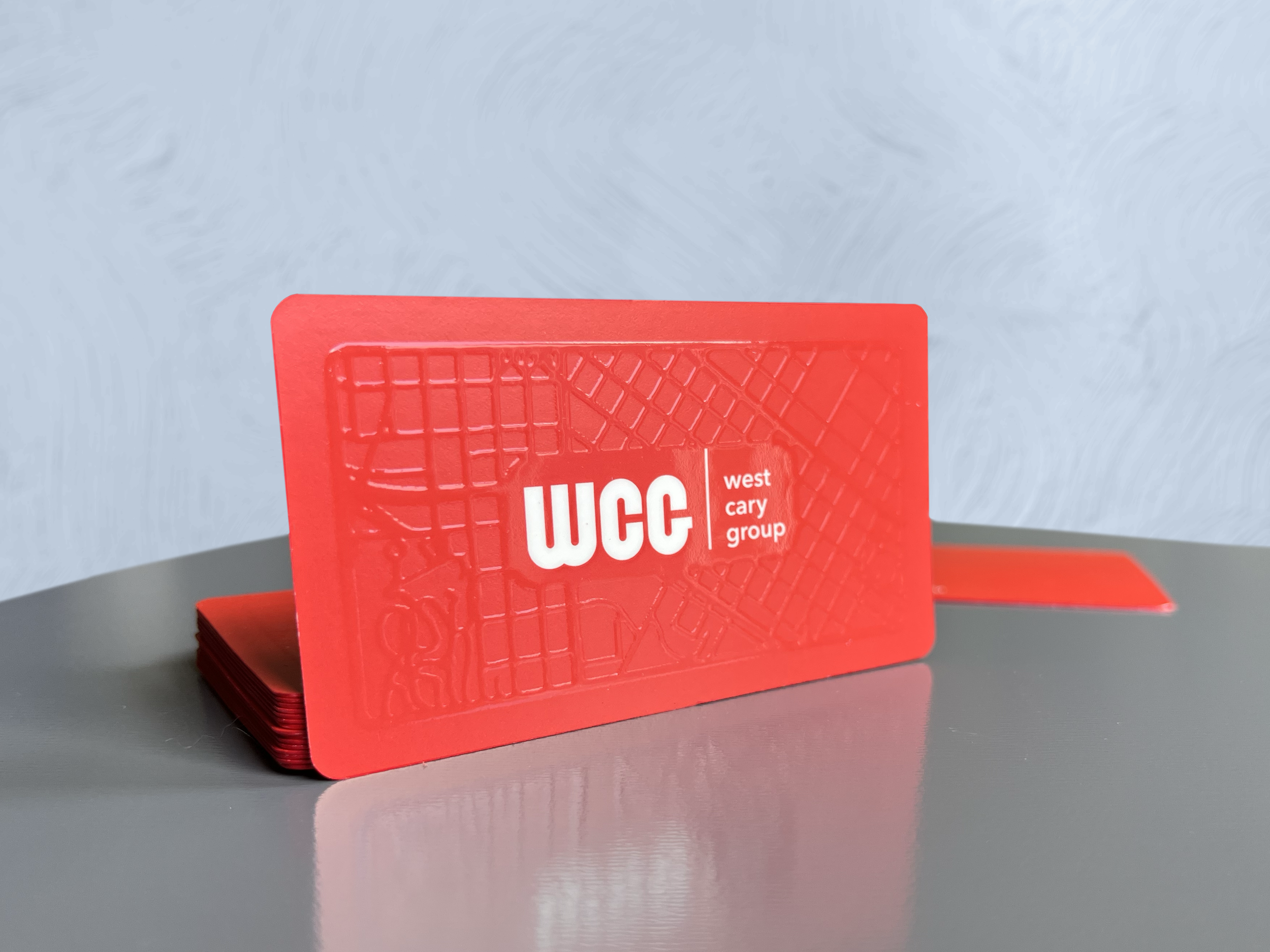 Stack of red plastic cards with the West Cary Group logo on the top card, featuring a map design in the background.