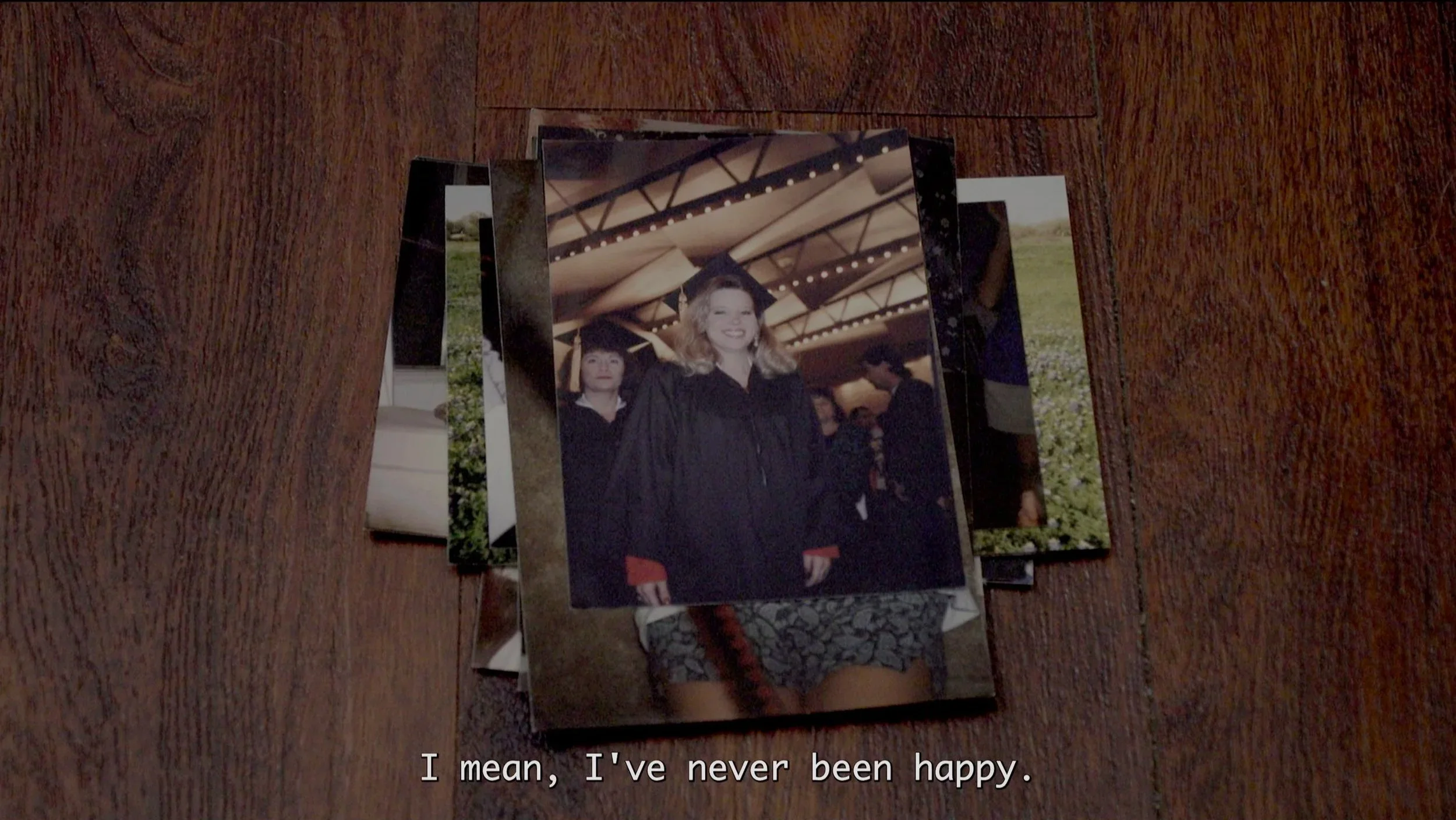 Stack of printed photographs on a wooden surface, with a woman in graduation gown smiling in one of the photos.