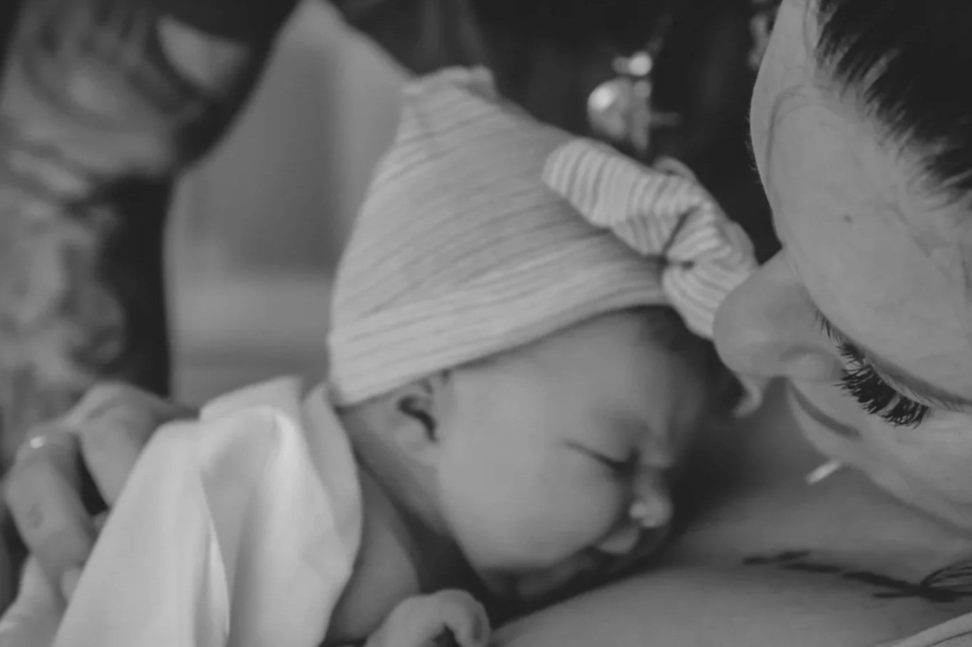 A woman warmly embraces a sleeping baby, resting her nose against the baby's forehead.