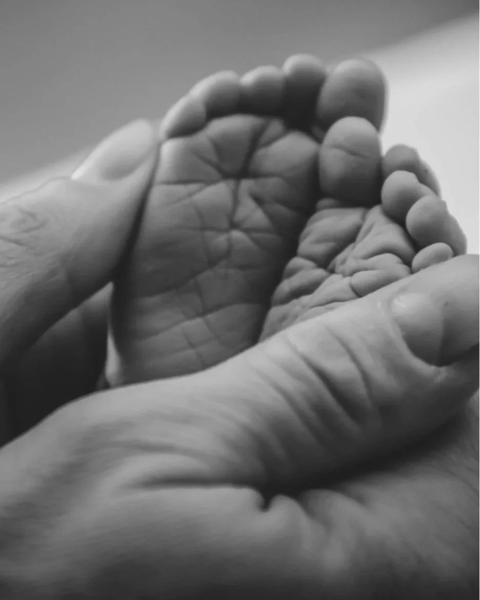 Close-up of a small child's tiny hand being gently held by an adult's hand in black and white.