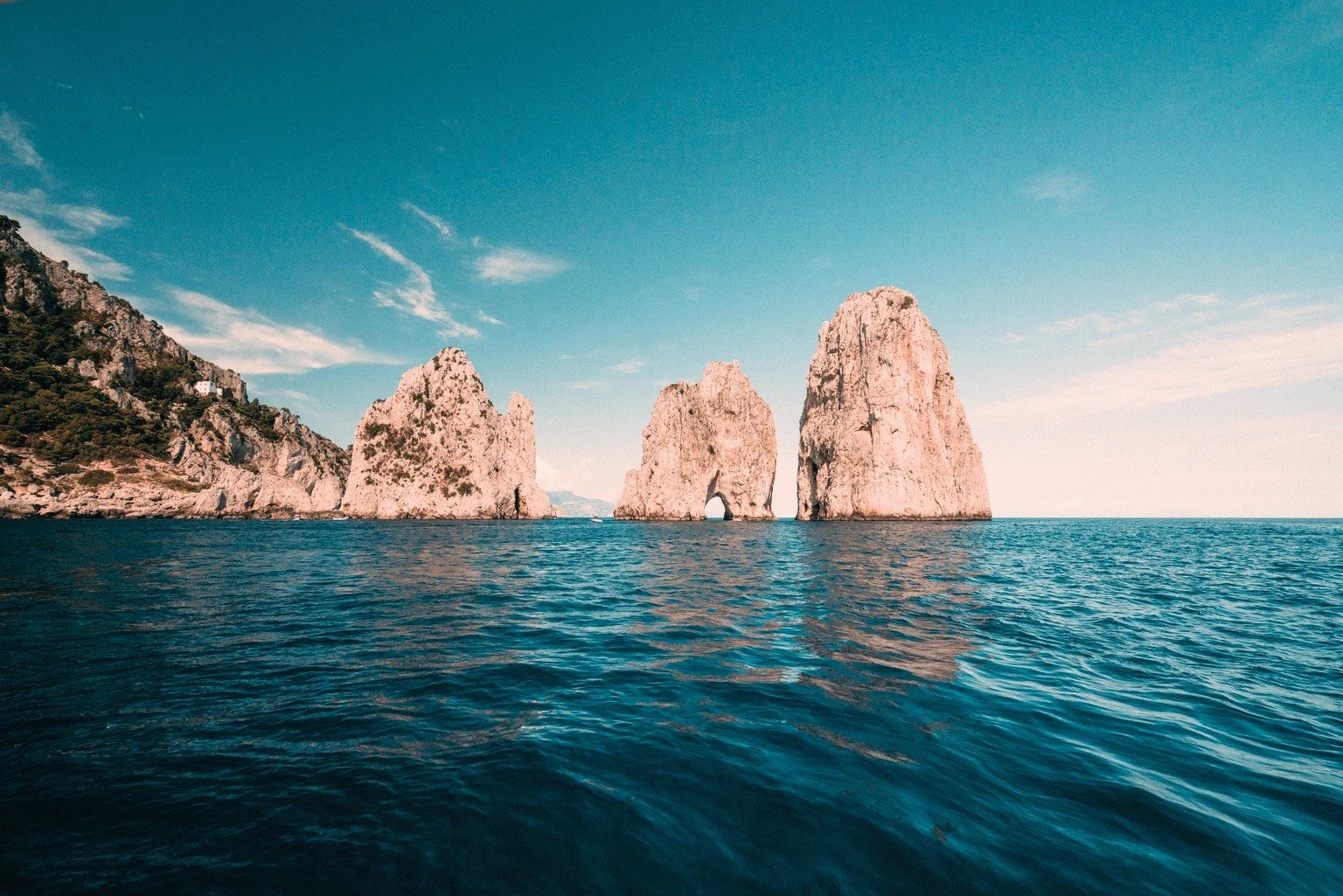 Sea stacks rising from the water with a rocky hillside on the left
