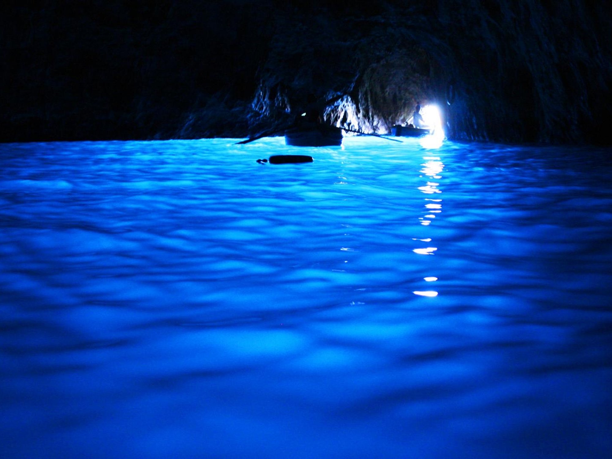 Inside a dark cave with bright blue water and a person in a kayak near the entrance.
