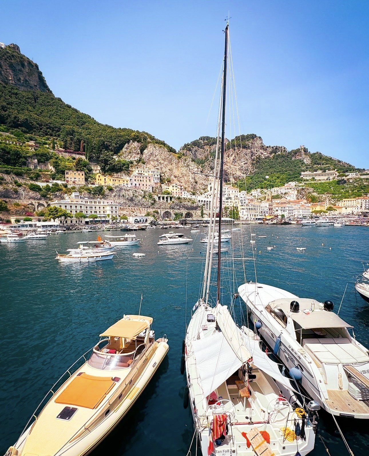 View of boats docked in a harbor with colorful buildings and green mountains in the background.