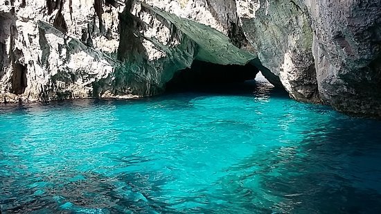 A turquoise water body flowing through a rocky cave with jagged stone formations.