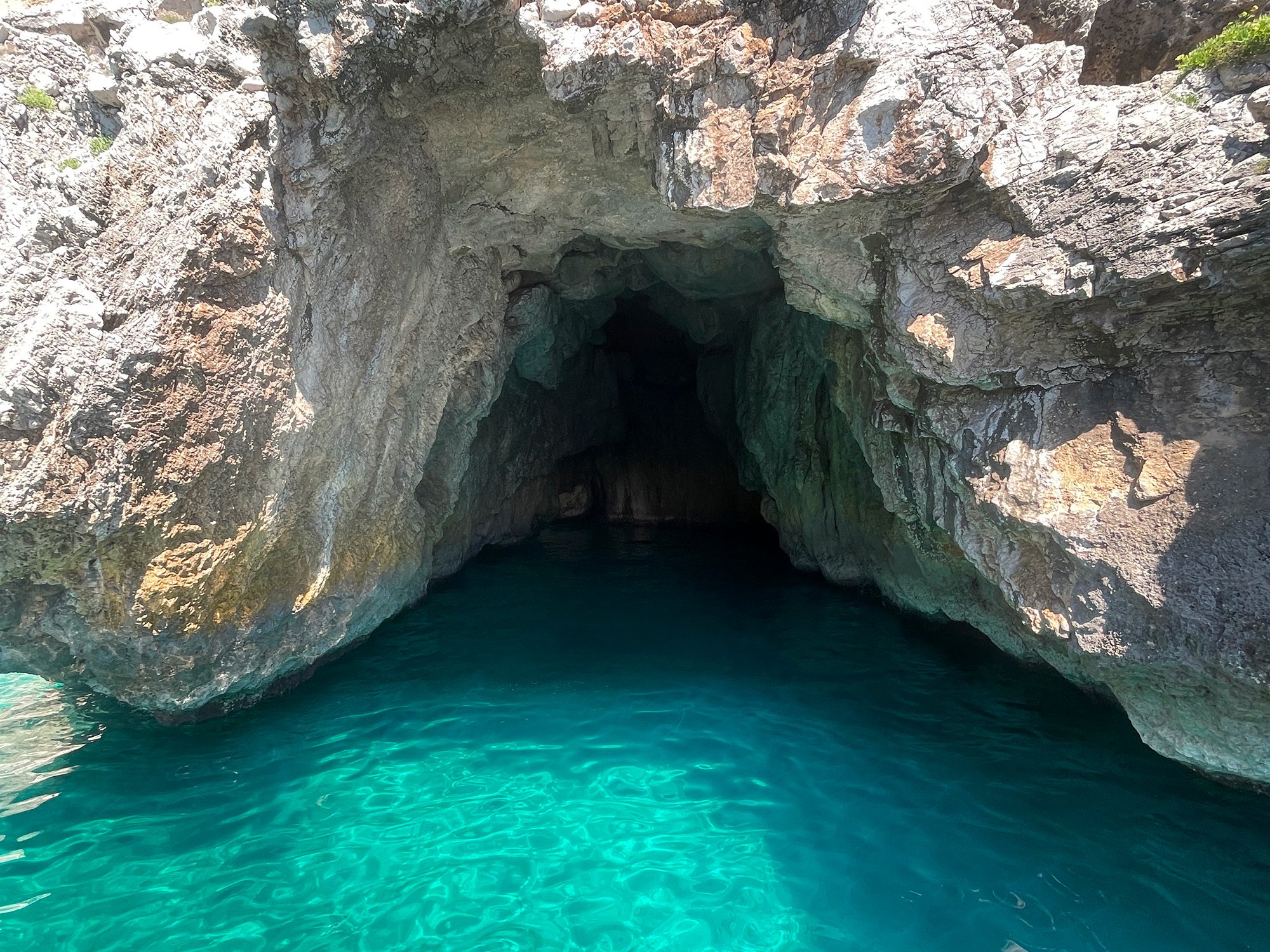 An entrance to a sea cave with turquoise water inside, surrounded by rocky cliffs with sunlight shining on the rocks.