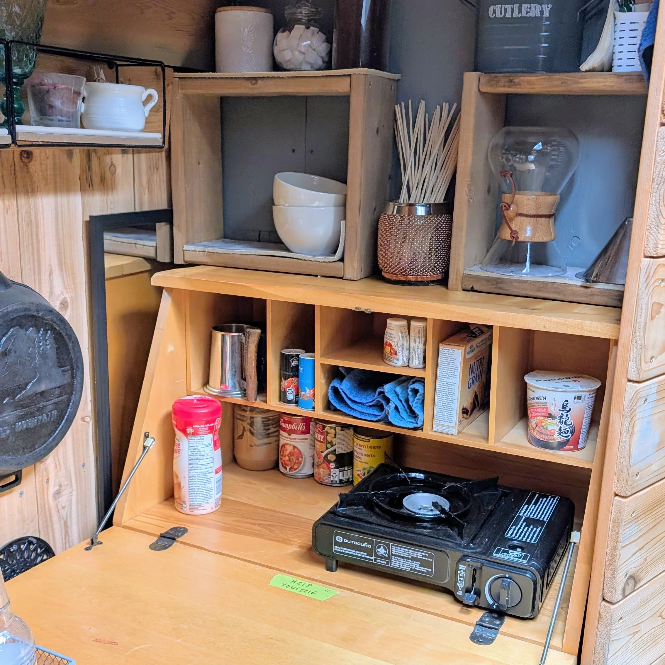 The interior of the fold out kitchen counter, a gas burner, coffee and tea supplies, dishes and a few snacks are visible.