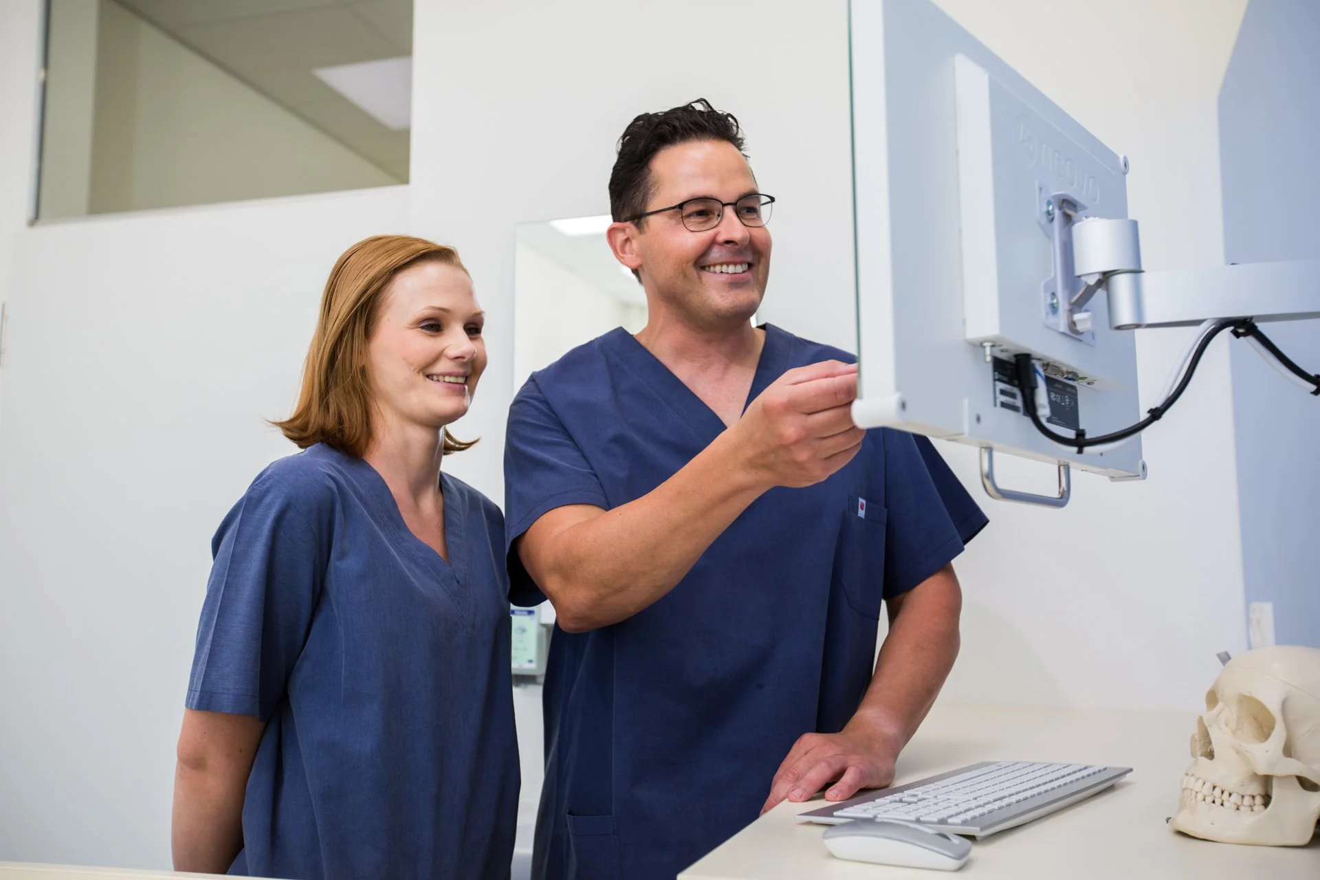Zwei medizinische Fachkräfte in blauer Klinik-Kleidung arbeiten mit einer medizinischen Maschine in einem Behandlungsraum.