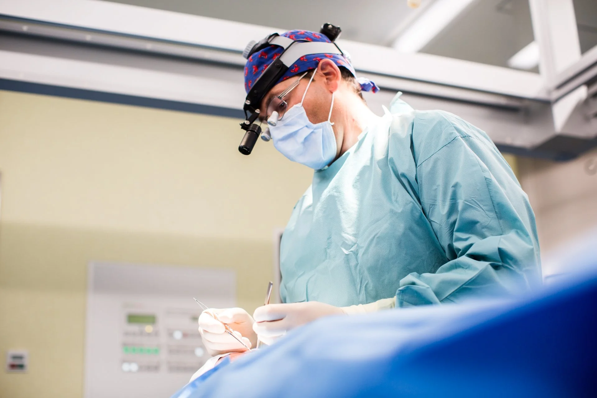 Chirurg in Operationsraum mit Schutzkleidung, Maske und Lupenbrille bei Operation