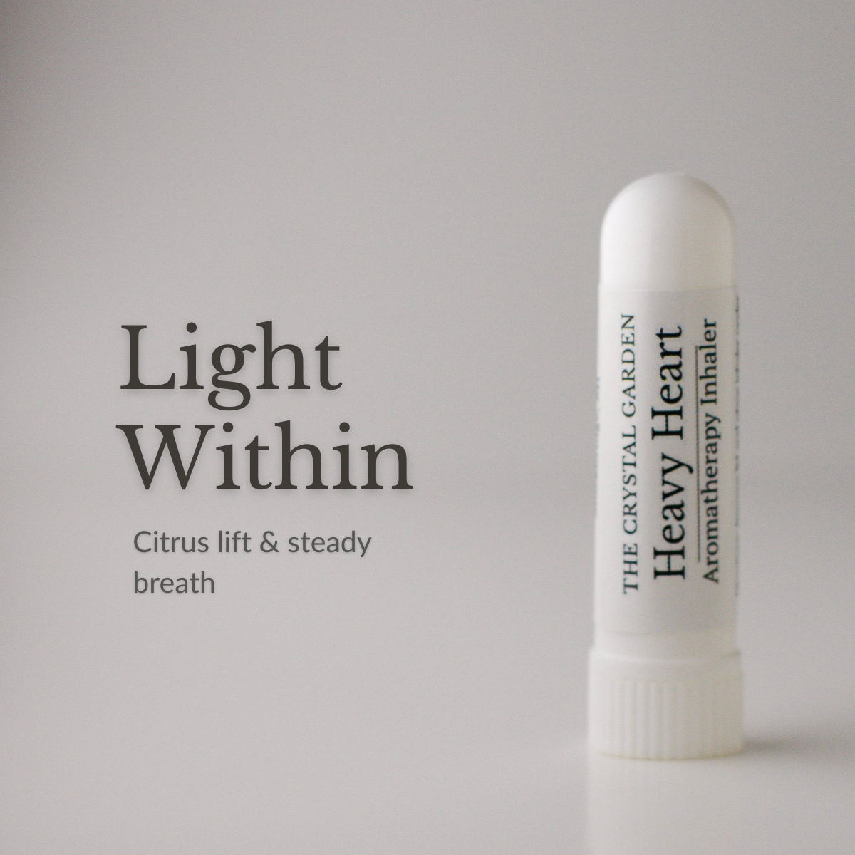 Heavy Heart aromatherapy inhaler standing on a neutral surface with soft linen, candlelight, and rose quartz in a calm reflective setting. light with in